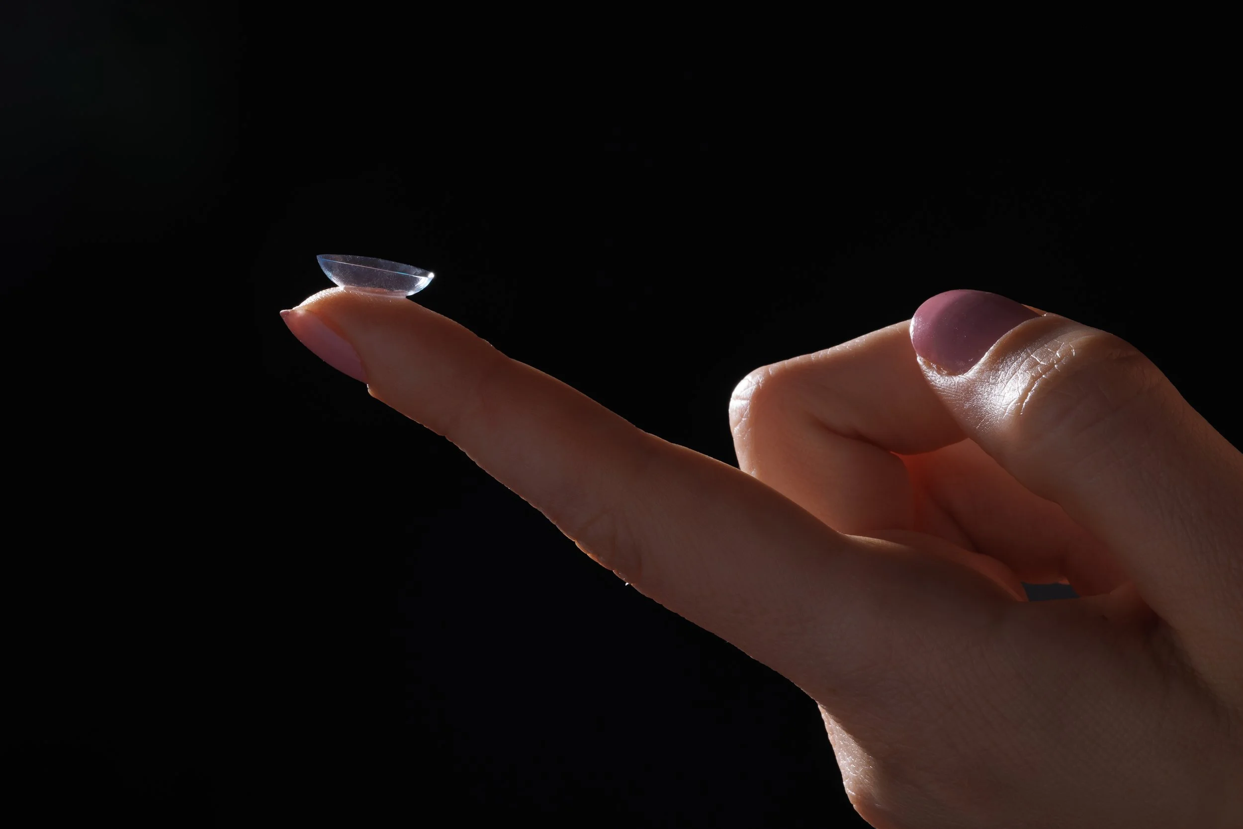 A hand holding a contact lens on the tip of the index finger against a black background | Dr. Robert Meade | Public Speaker & Vision Consultant | Presentations about Eyes and Vision