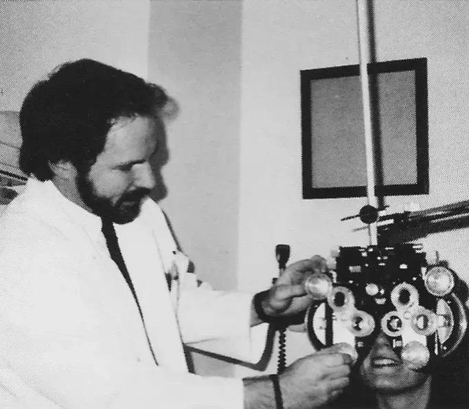 Black and white photo of a male optometrist performing an eye exam with a phoropter | Dr. Robert Meade | Public Speaker & Vision Consultant | Presentations about Eyes and Vision