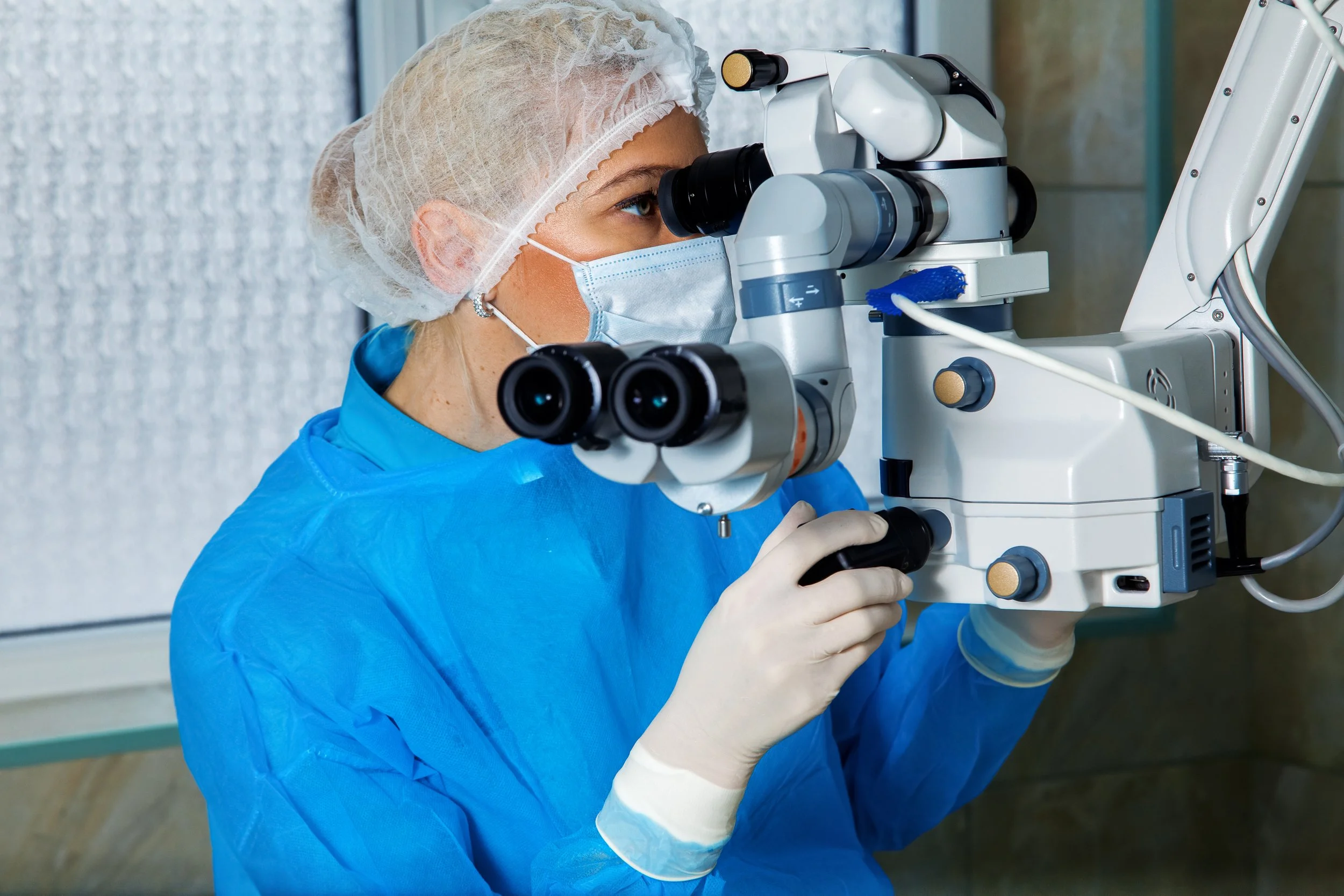 A female medical professional wearing scrubs, gloves, a face mask, and a hairnet, examining through a microscope | Dr. Robert Meade | Public Speaker & Vision Consultant | Presentations about Eyes and Vision