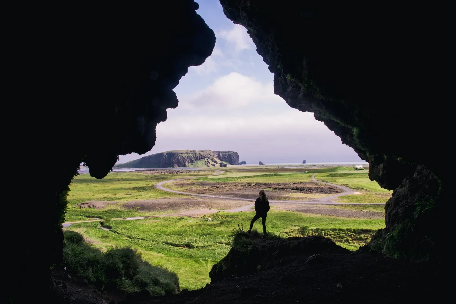 A photographer standing in a cave mouth looking out over green coastal plains