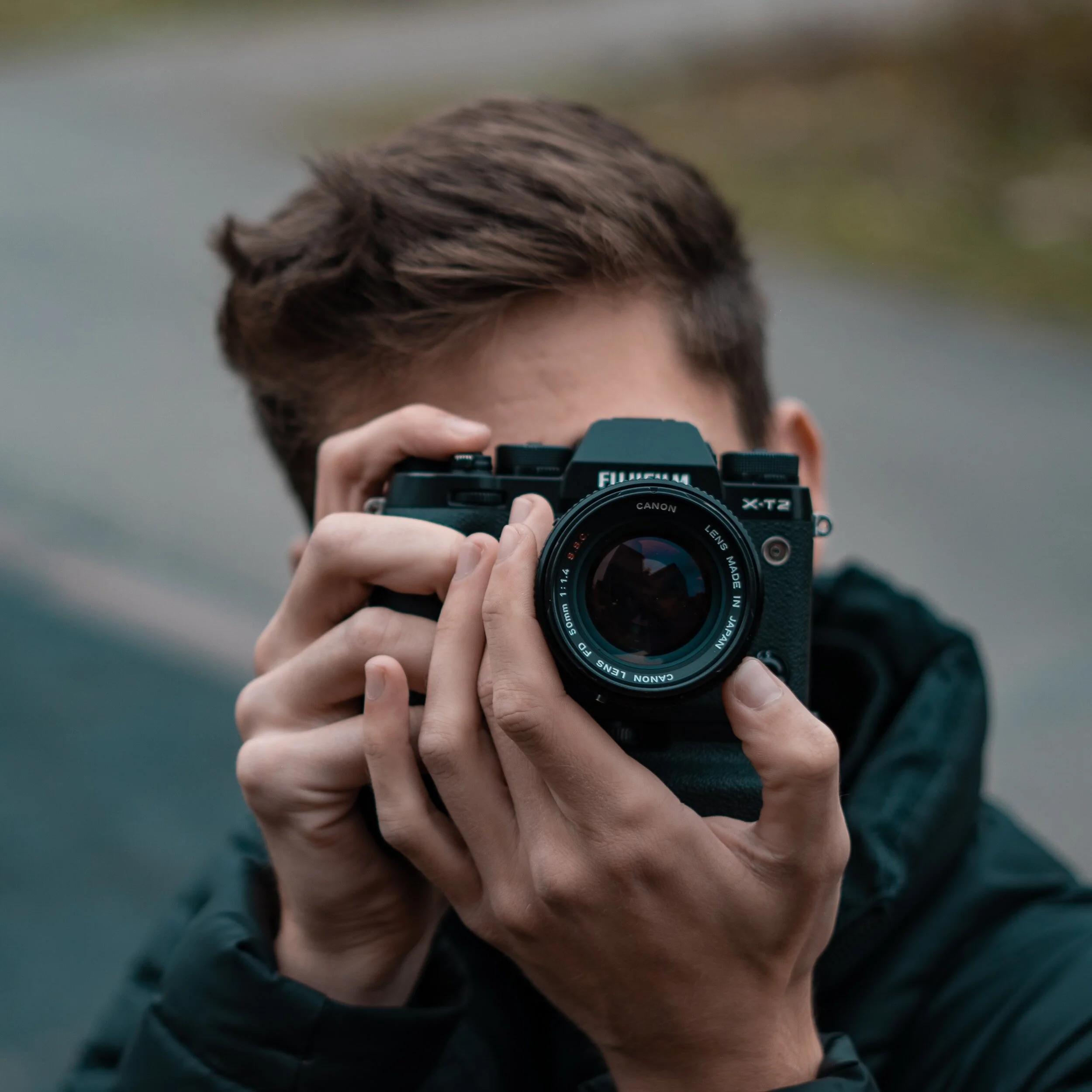 A man raising a mirrorless camera to his eye, facing towards the viewer.