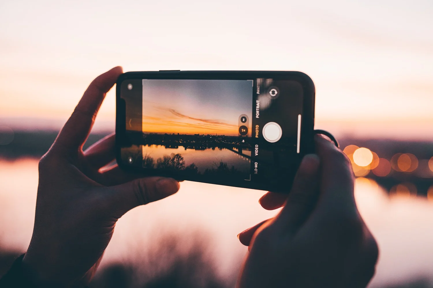 A phone held up to photograph a sunset over the water