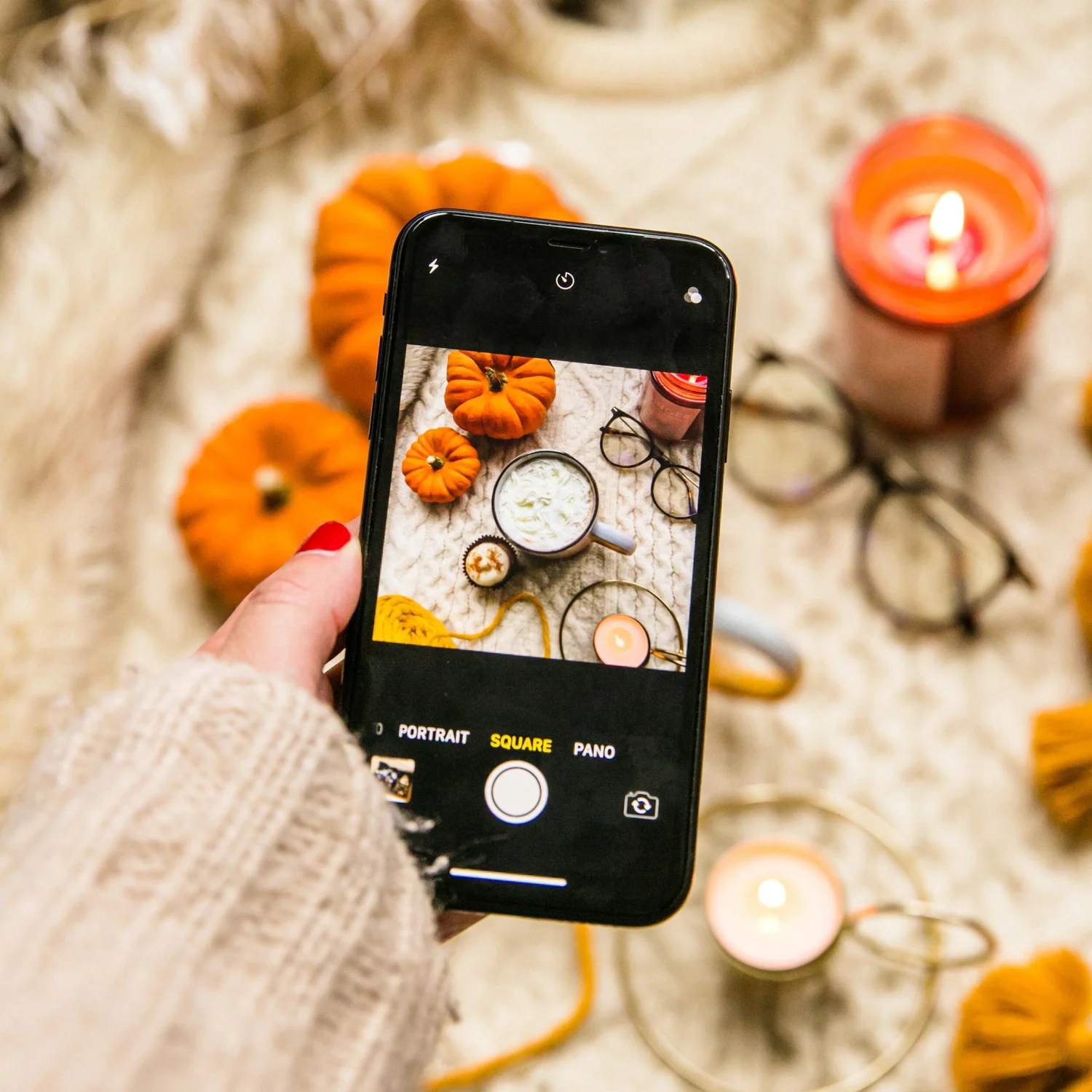A phone photographing pumpkins and candles in warm autumn light