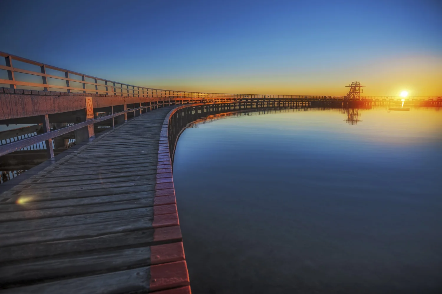 A pier stretching into still water at dusk