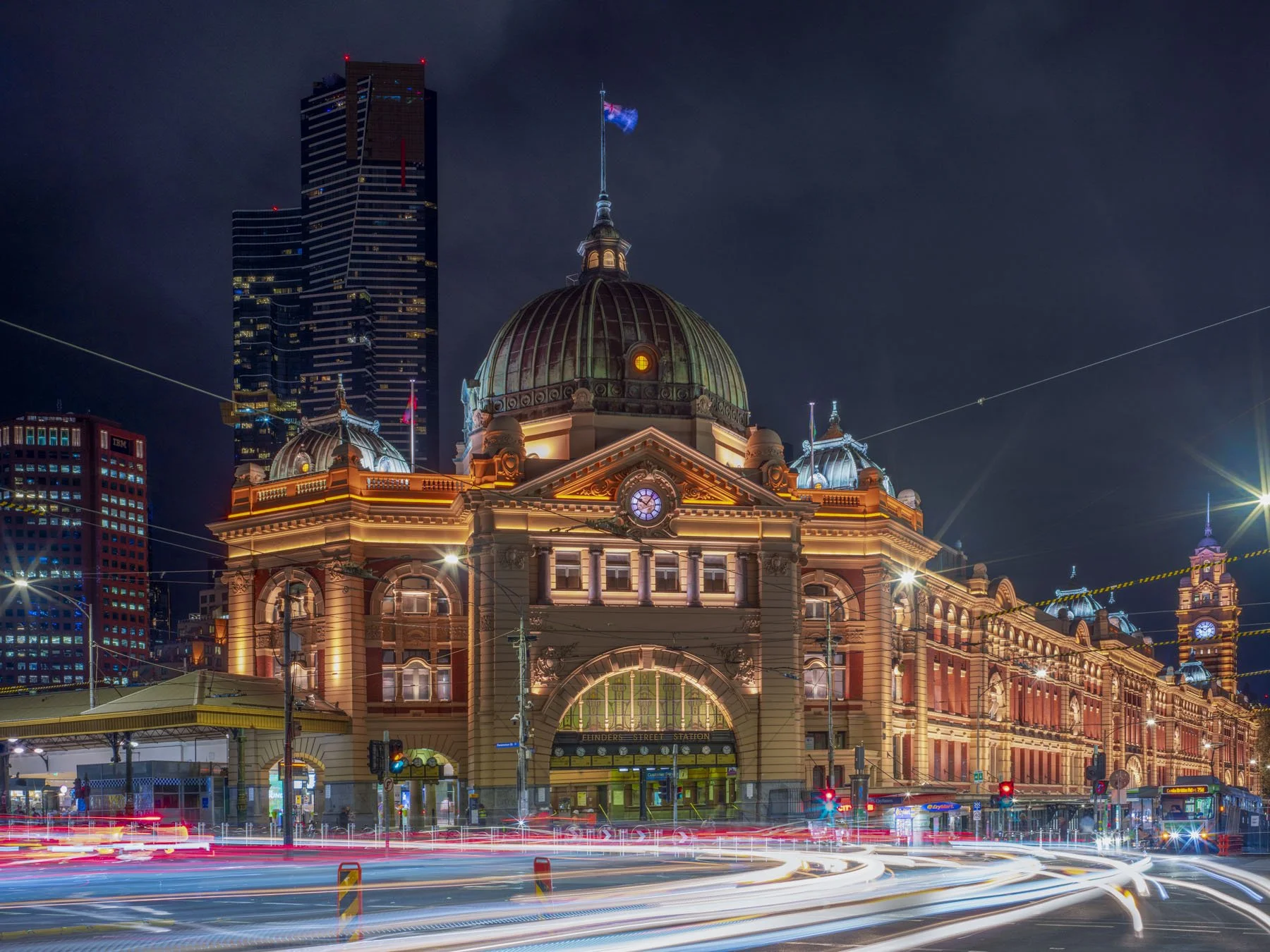 Flinders Street Station lit up at night with light trails from passing trams