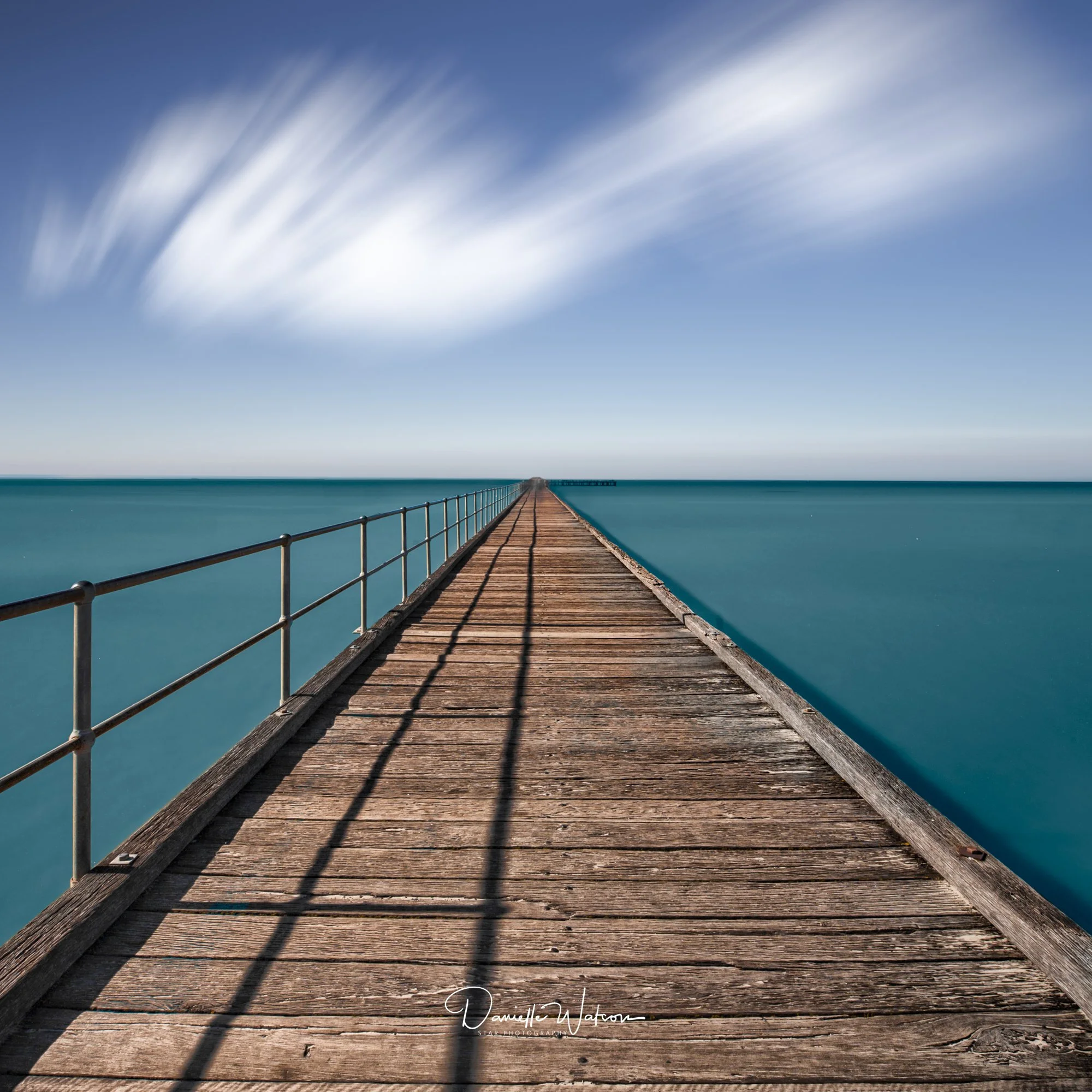 Long exposure of a timber pier over smooth blue water