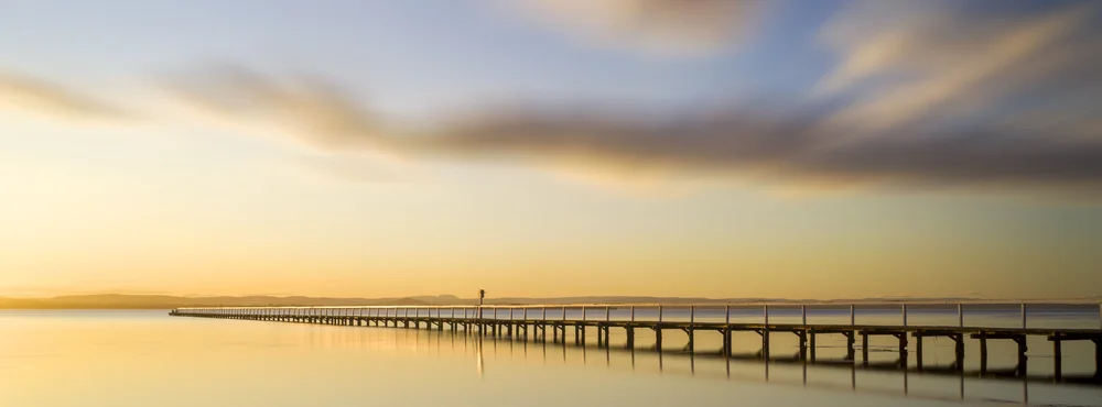 A long timber pier stretching into calm water at sunset