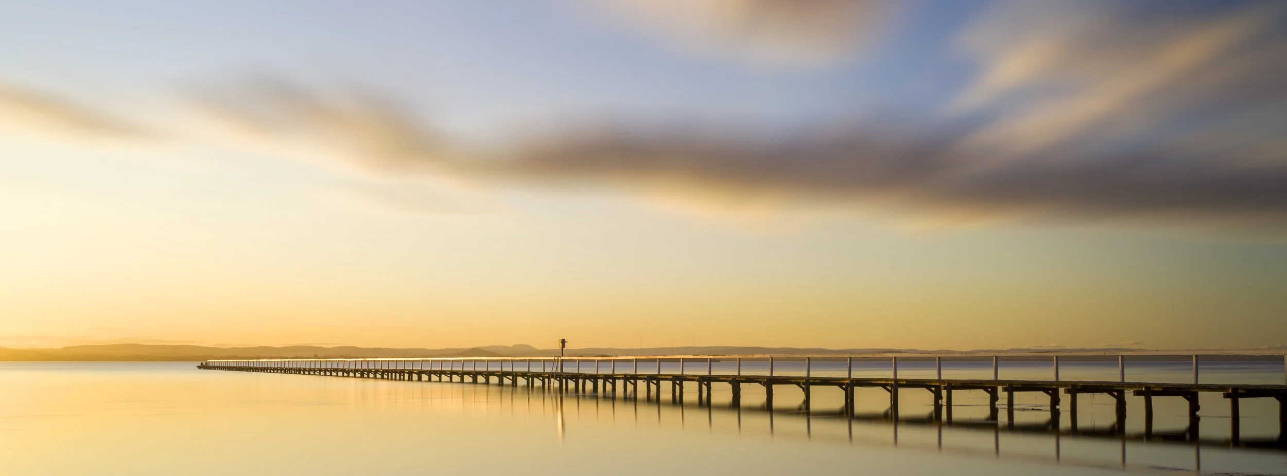 A long timber pier stretching into calm water at sunset