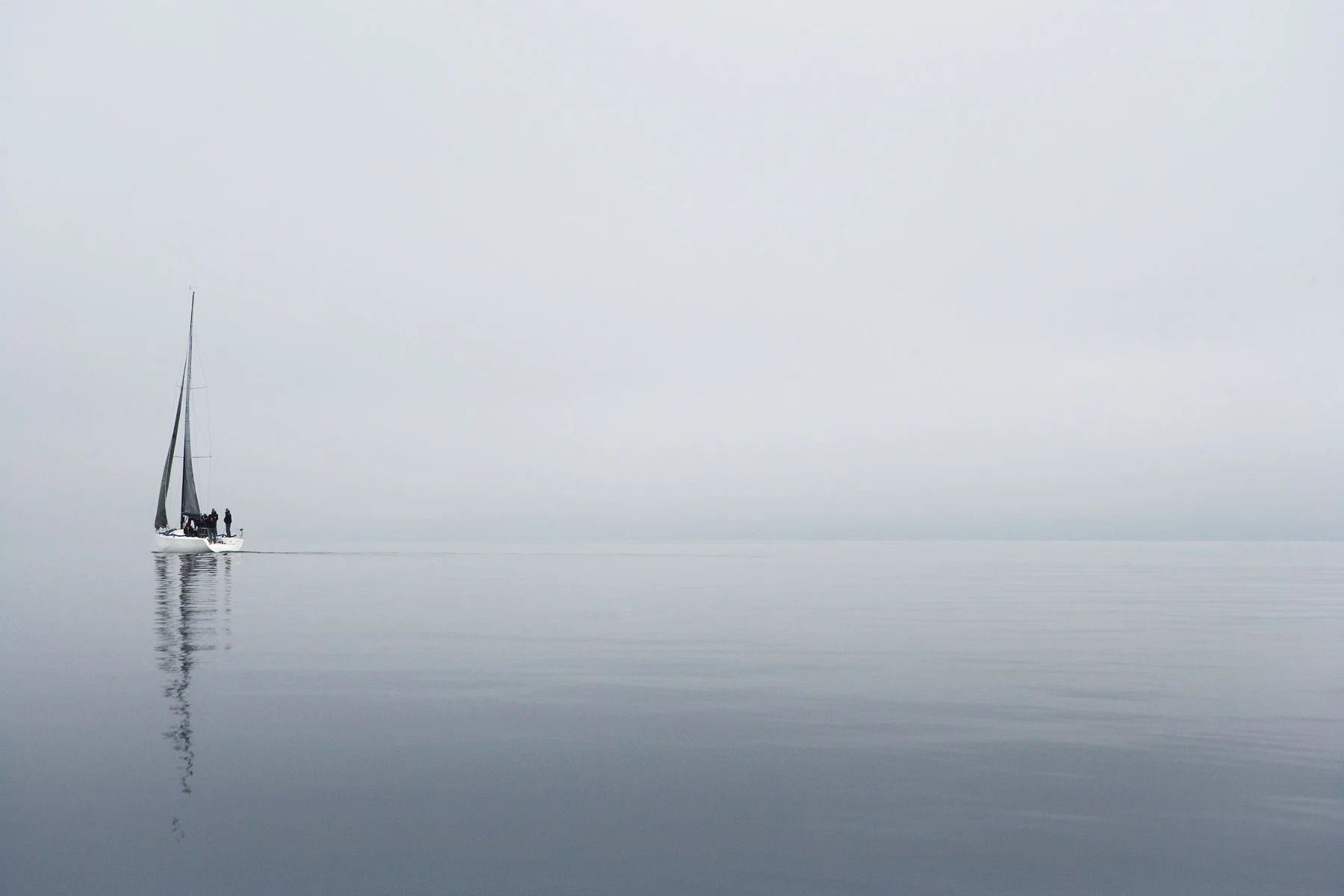 A lone sailboat on calm, misty water