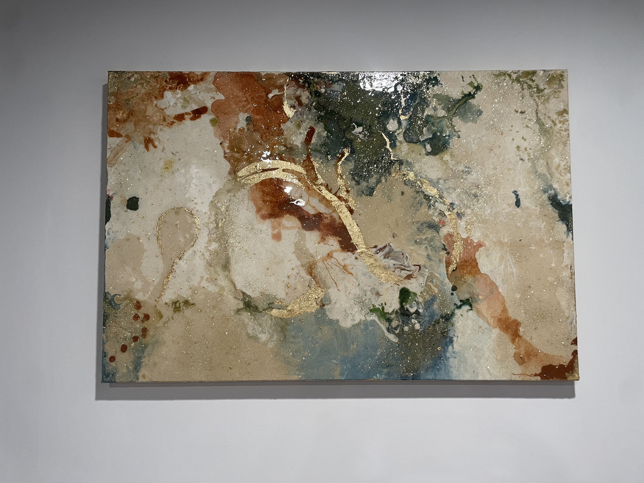 Abstract painting with splashes of gold, beige, brown, blue, and green colors on a rectangular canvas.