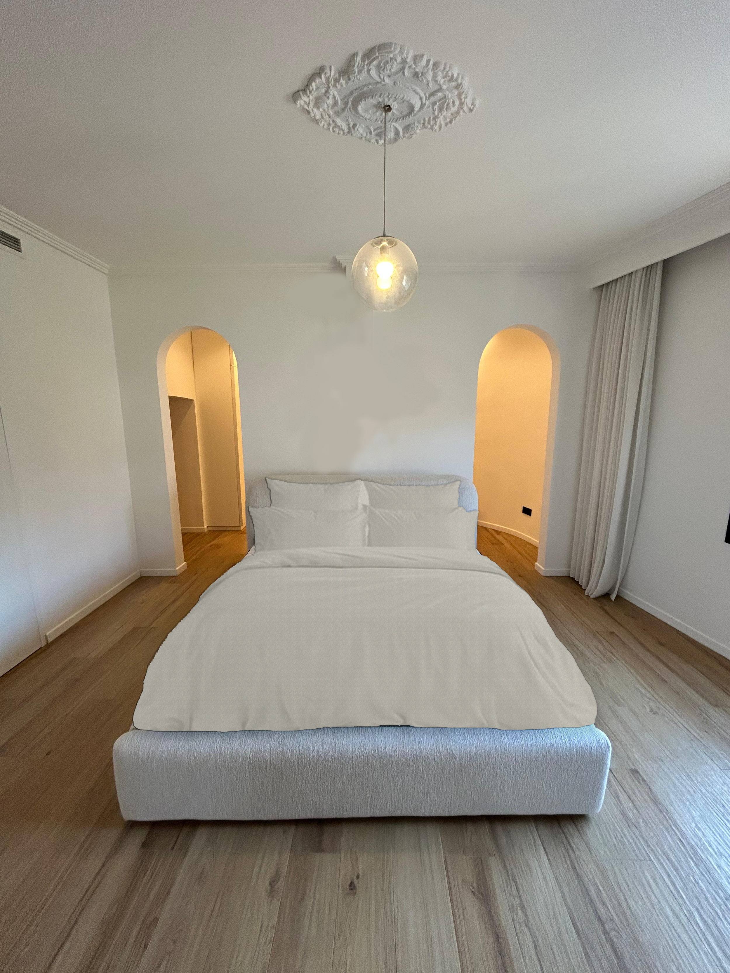 The master bedroom embodies a serene and cohesive design, with the bed positioned against a central wall that discreetly conceals the walk-in closet. Two symmetrical arches on either side of the wall serve as elegant passageways, seamlessly guiding m