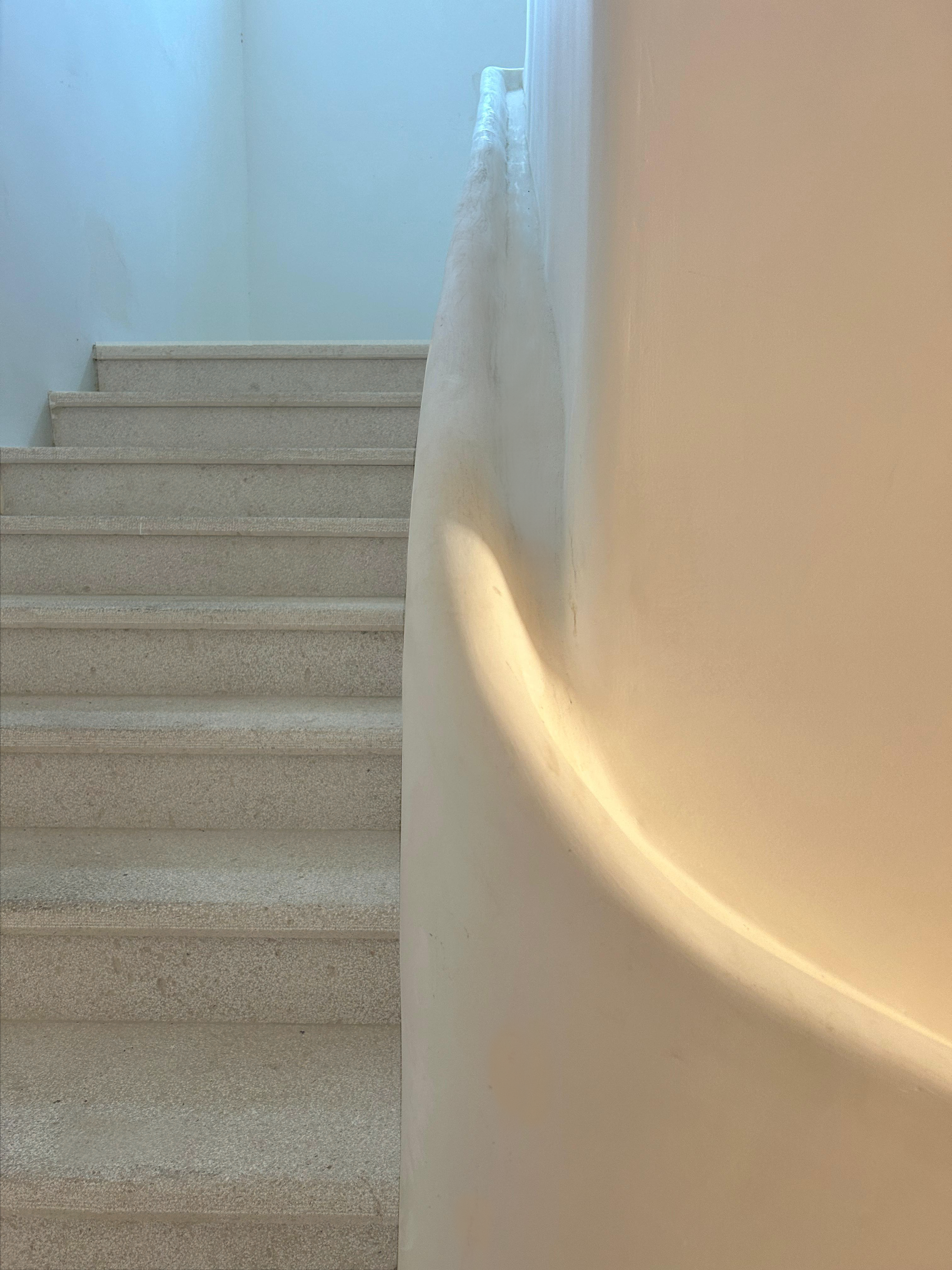 The staircase features a seamlessly integrated curved railing that flows organically from the wall, enhancing the minimalist aesthetic with its sculptural form while providing both functional support and a harmonious connection to the architecture