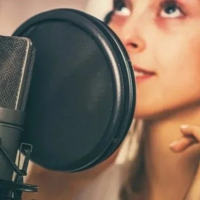 Person recording voice in a home studio with a microphone and pop filter.