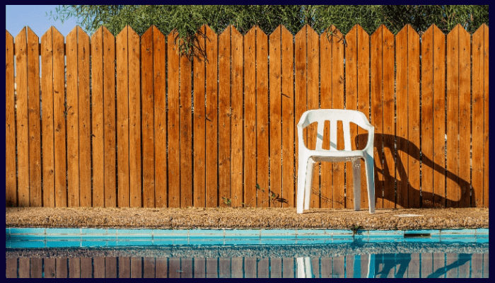 Backyard swimming pool with tall timber privacy fence providing wind protection and seclusion.