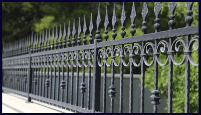 Black wrought iron fence with spear tops and scrollwork, installed in a landscaped front yard to enhance security and classical street appeal.