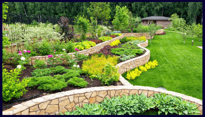 Landscaped backyard with tiered stone retaining walls, colourful garden beds, and a lush green lawn, showcasing a well-planned and aesthetically pleasing design.
