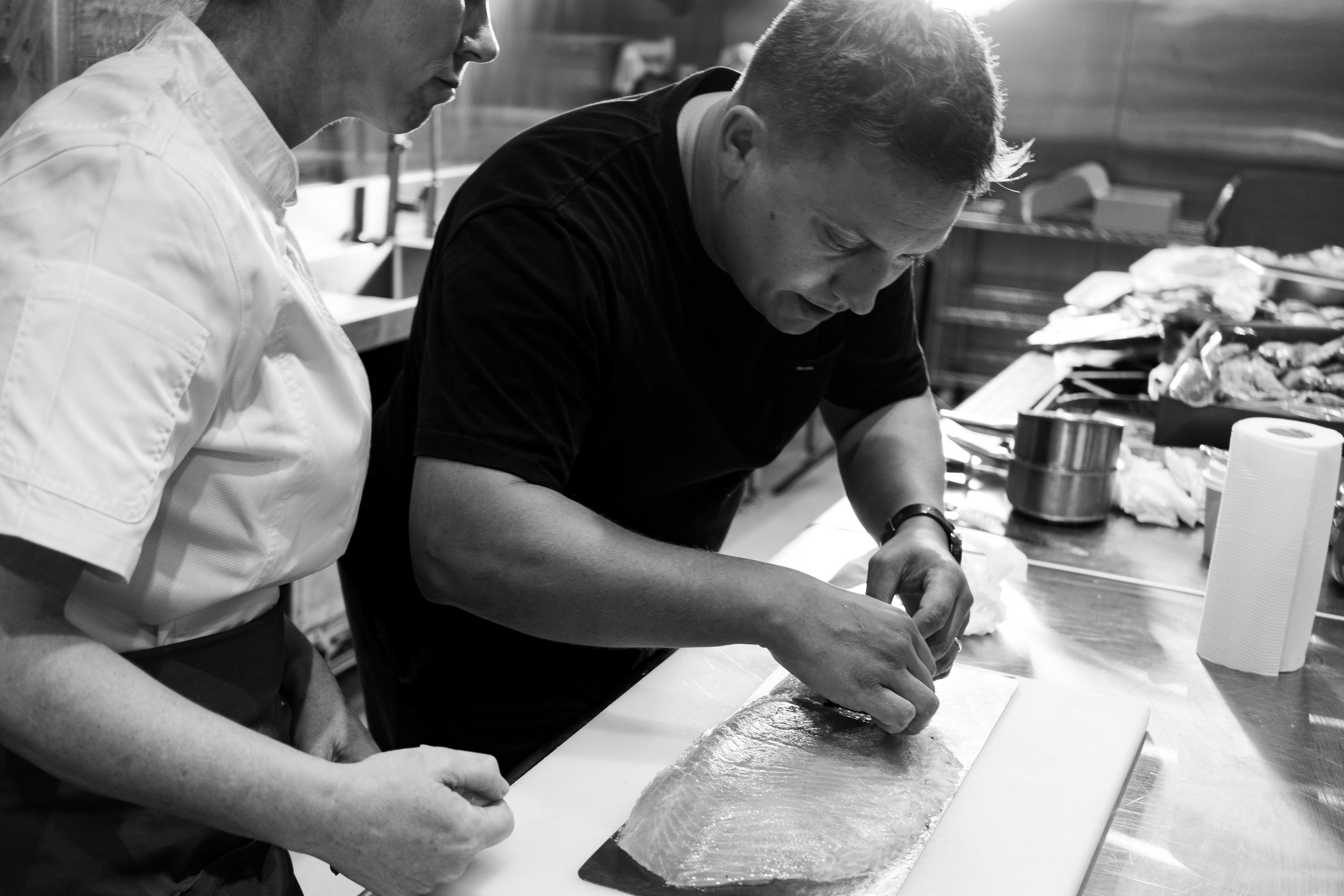 Two chefs preparing fish in a kitchen, focusing on filleting.
