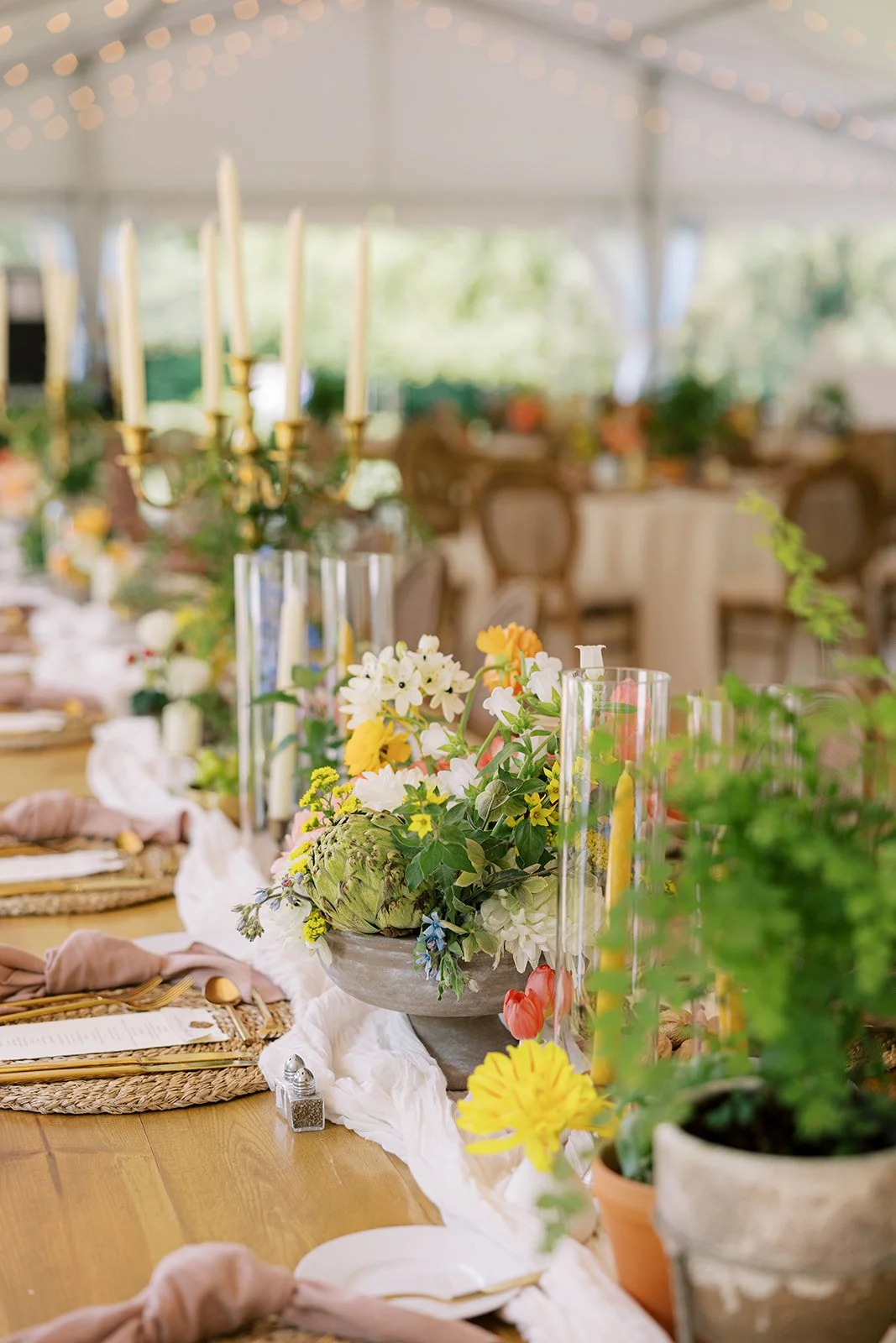 A decorated table at an event with floral centerpiece, candles, and place settings under string lights.