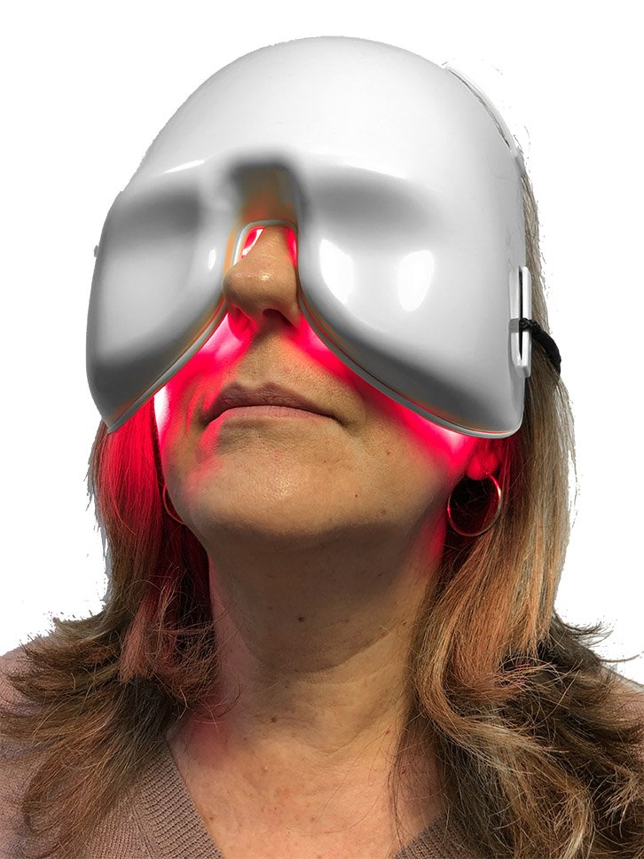 A woman wearing a dry eye mask with red light therapy, illuminated in red, on her face.