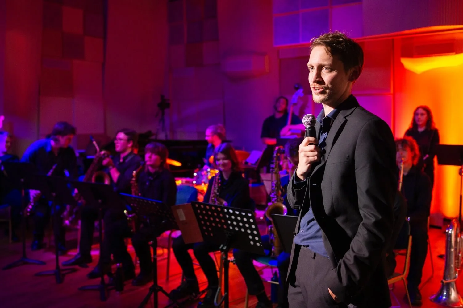 Alex Thomas-French addresses audience in front of youth big-band performance.