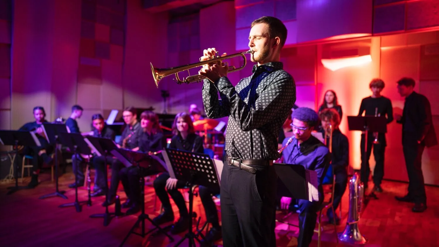 Lead trumpet takes solo with band behind under vibrant lighting.