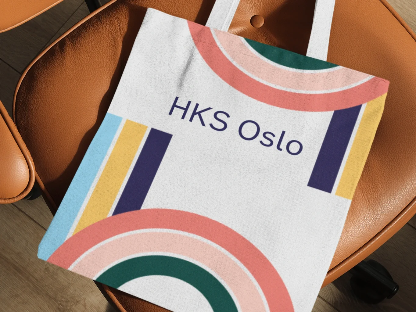 A colorful and geometrically designed desk folder with the text 'HKS Oslo' placed on a brown chair with wooden legs.