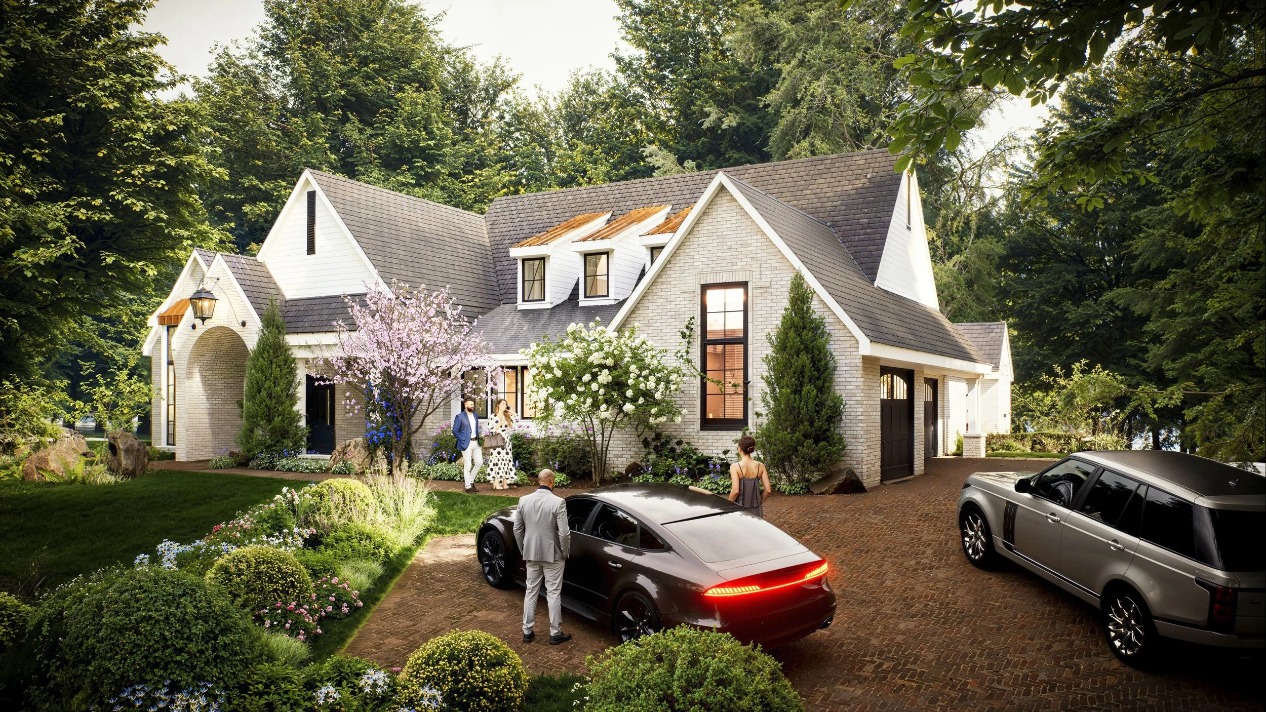 Discover our elegant white brick cottage-style residence rendering, featuring a slate roof with copper accents, lush landscaping, and a classic herringbone brick driveway.