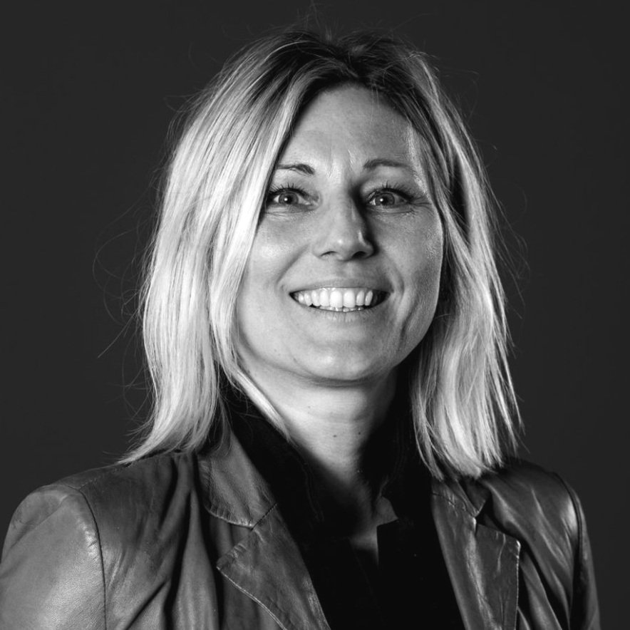 Black and white portrait of a woman with shoulder-length blonde hair, smiling, wearing a leather jacket.