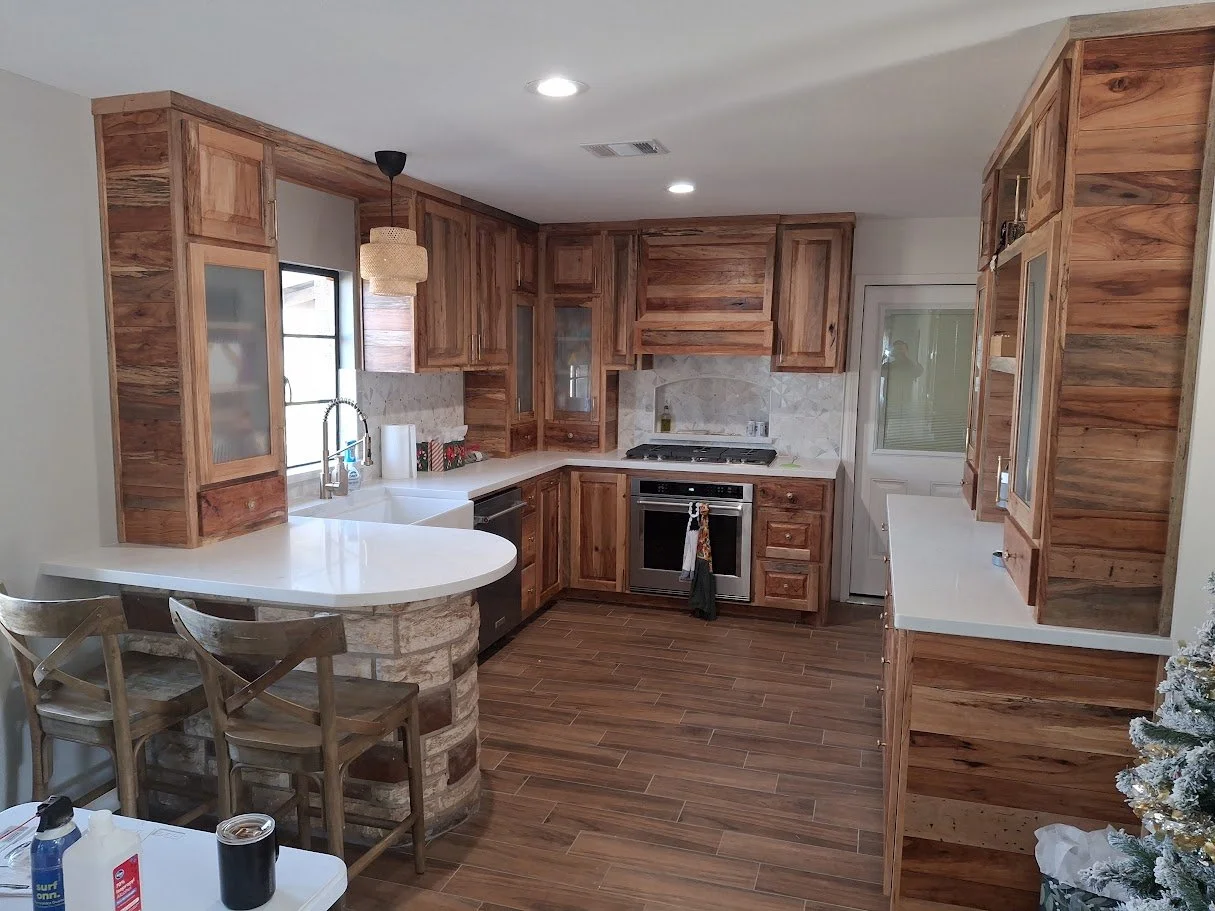 Custom kitchen featuring handcrafted rustic wood cabinetry built by Greywolf Cabinets and More, white quartz countertops, a curved stone bar island, and matching barstools.