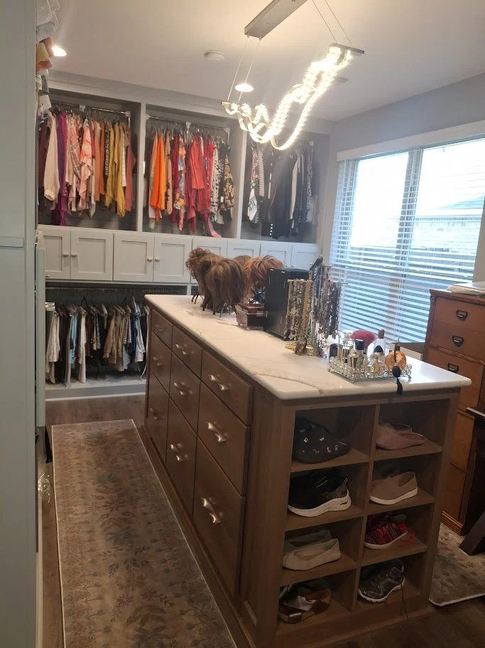 Custom walk-in closet built by Greywolf Cabinets and More, featuring built-in hanging storage, drawers, a central stone-topped island with shoe cubbies, and modern lighting.
