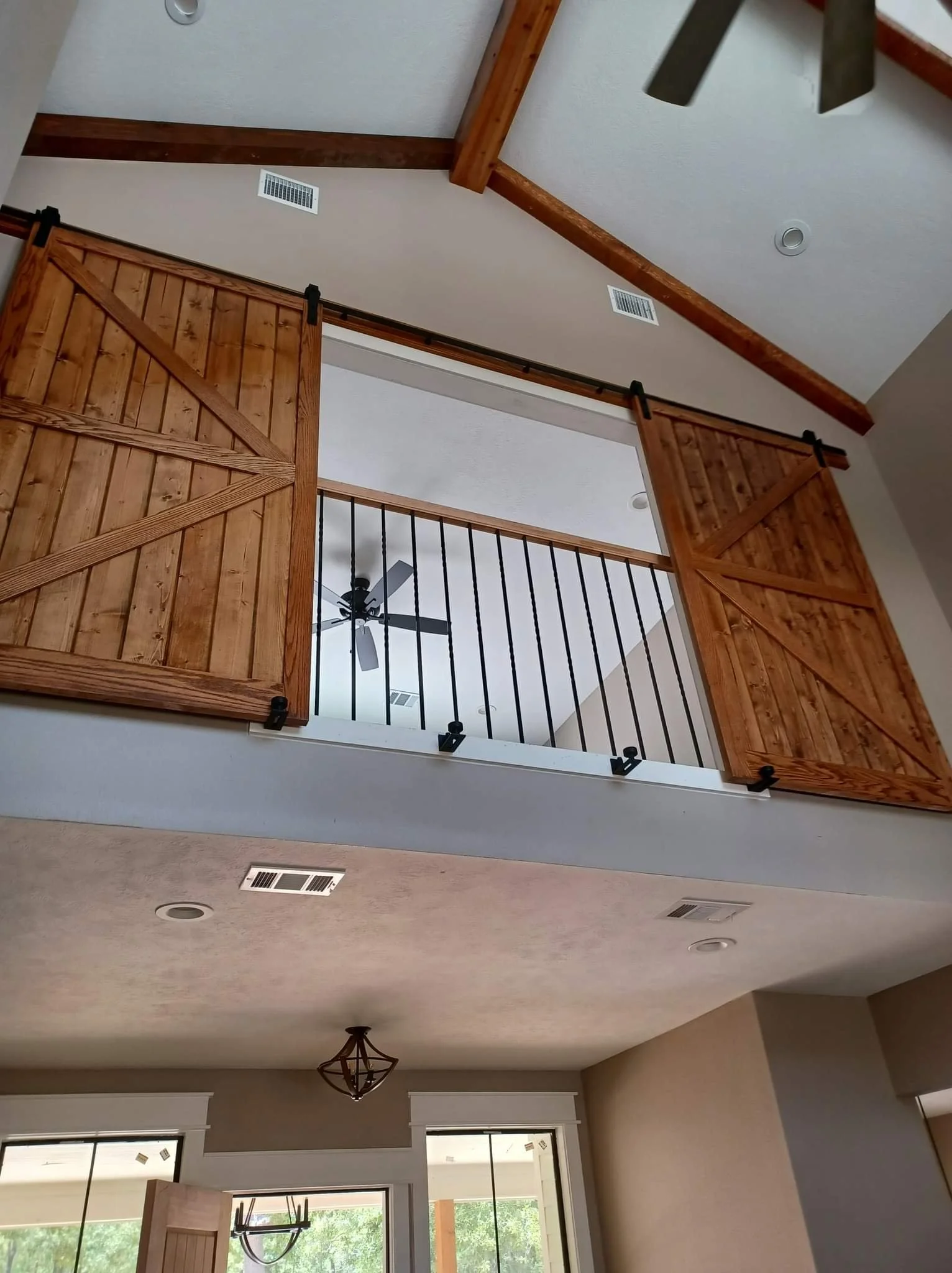 Custom interior wooden sliding barn doors built by Greywolf Cabinets and More, installed on a second-story loft opening with black hardware above a vaulted ceiling.