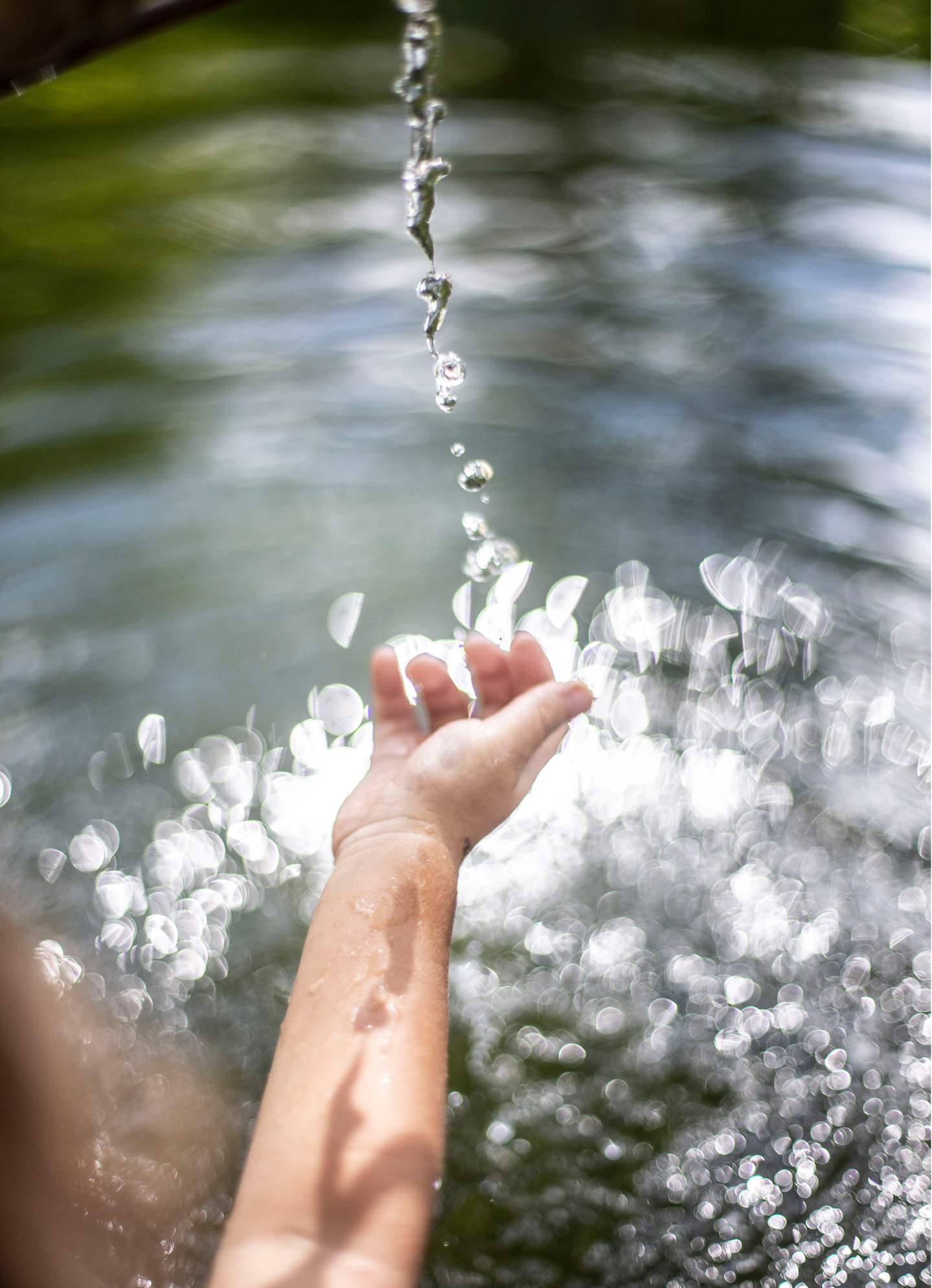 Hand fängt Wassertropfen auf, während sich das Licht in ihnen spiegelt.
