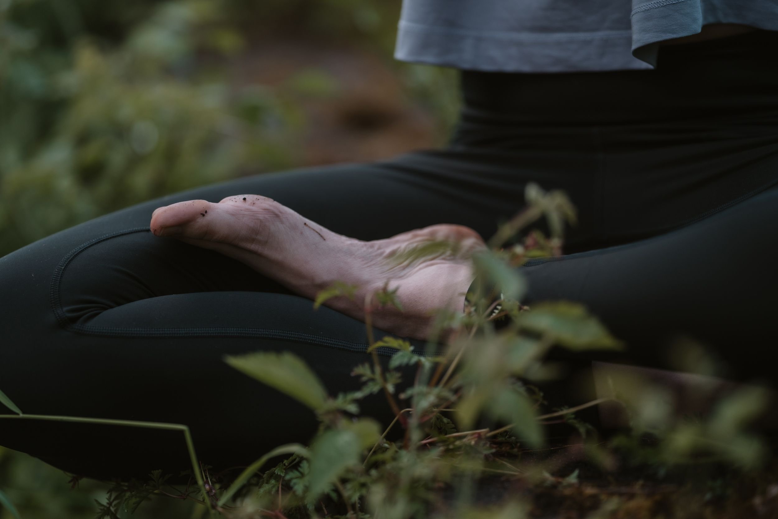 Frau sitzt im Schneidersitz auf dem Waldboden.