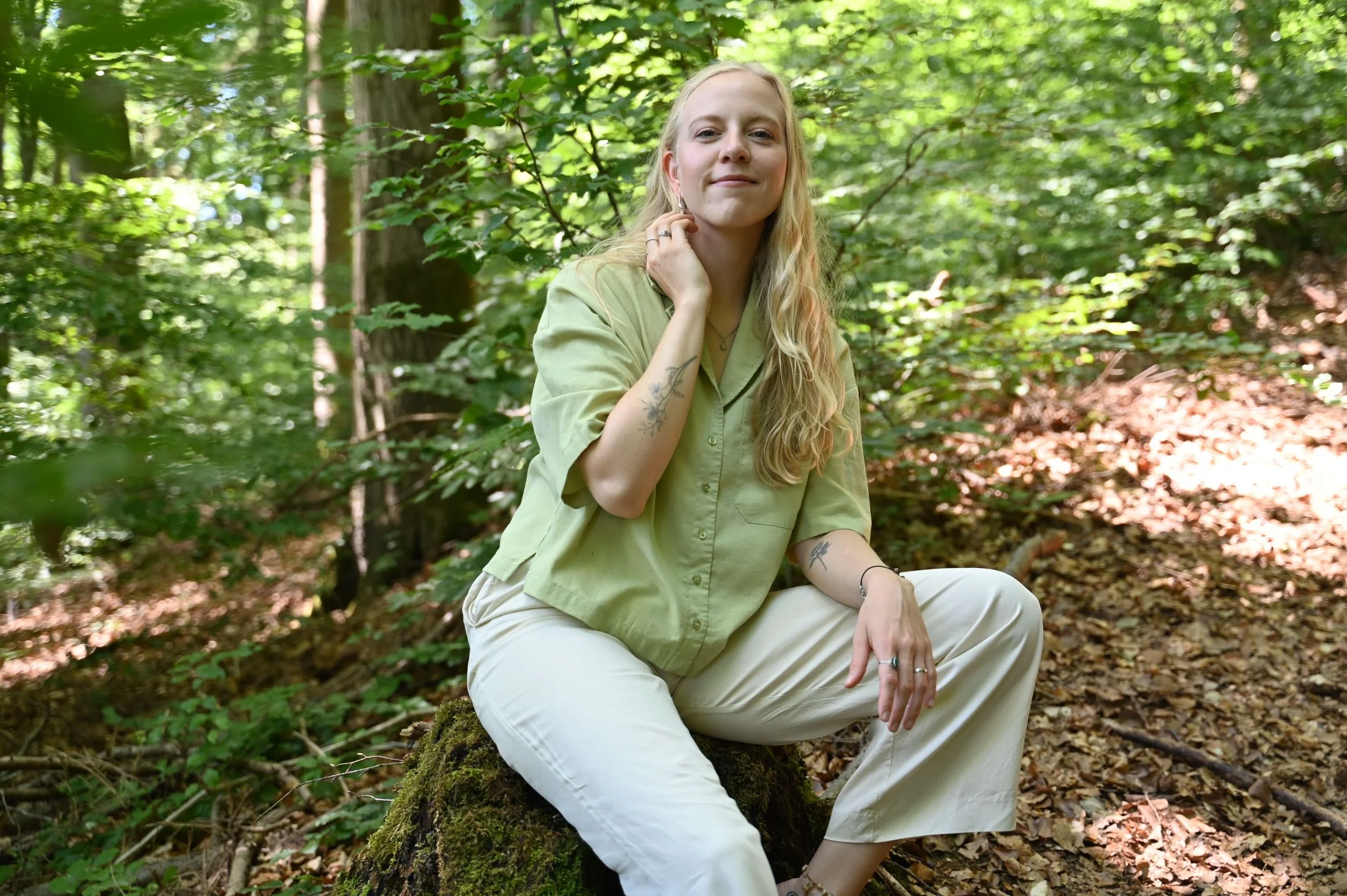 Leona Roes sitzt im Wald auf einem Baumstamm.