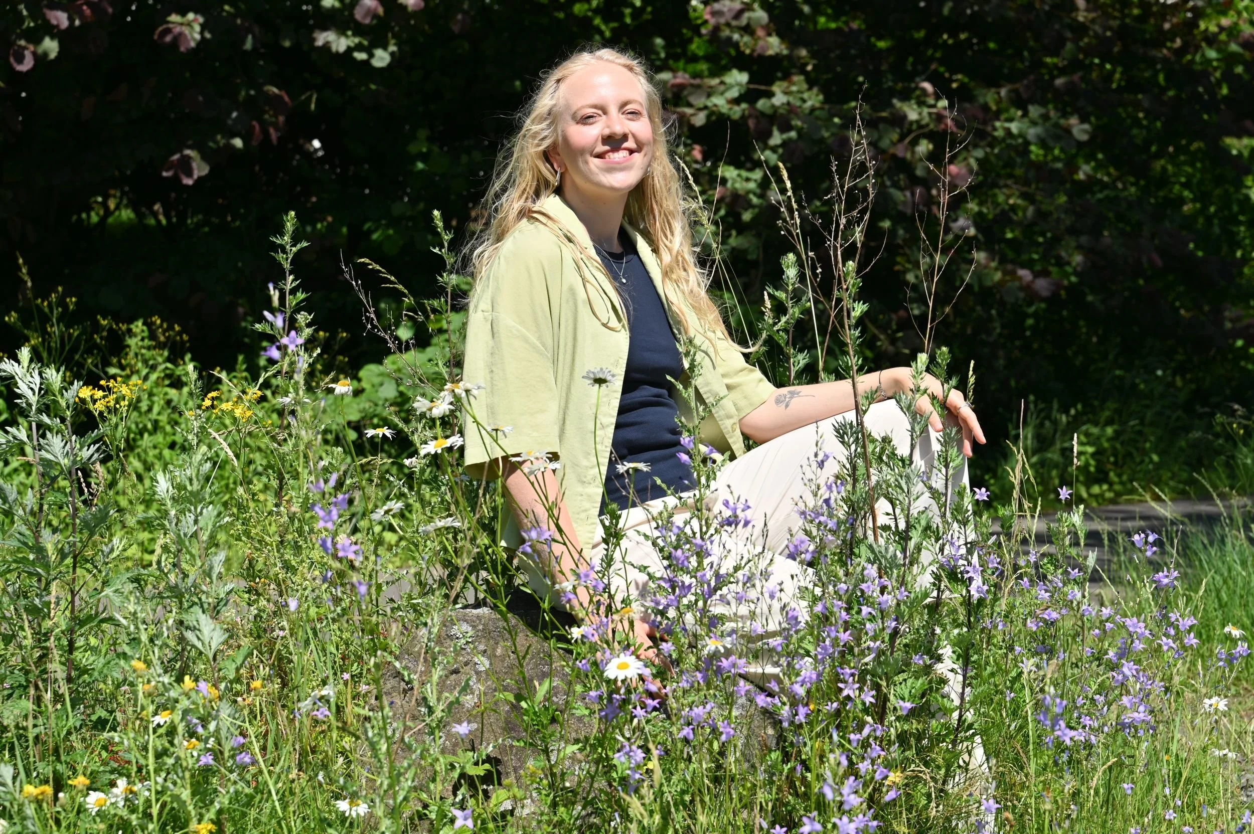 Frau sitzt auf einem Stein in einer bunten Blumenwiese.