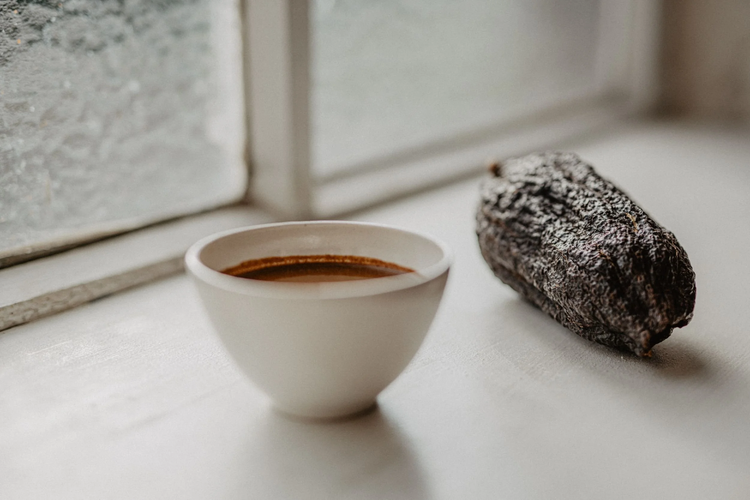 Tasse mit zeremoniellem Kakao und Kakaobohne vor einem Fenster.
