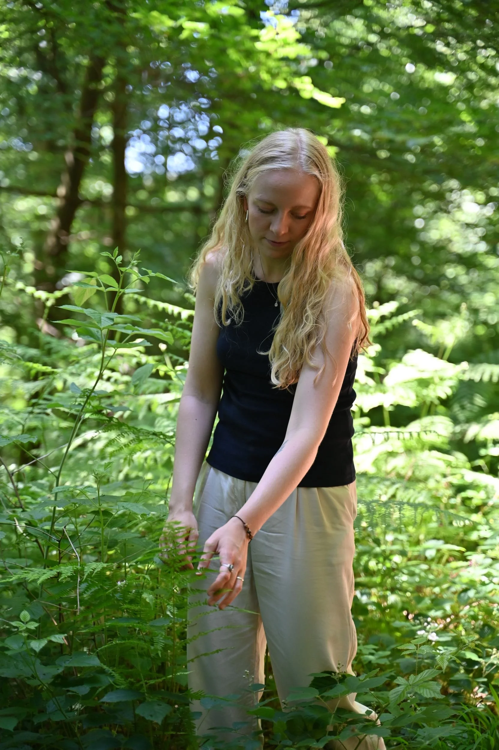 Frau im Wald, die achtsam Farne und Pflanzen berührt und ganz im Moment die Natur genießt.