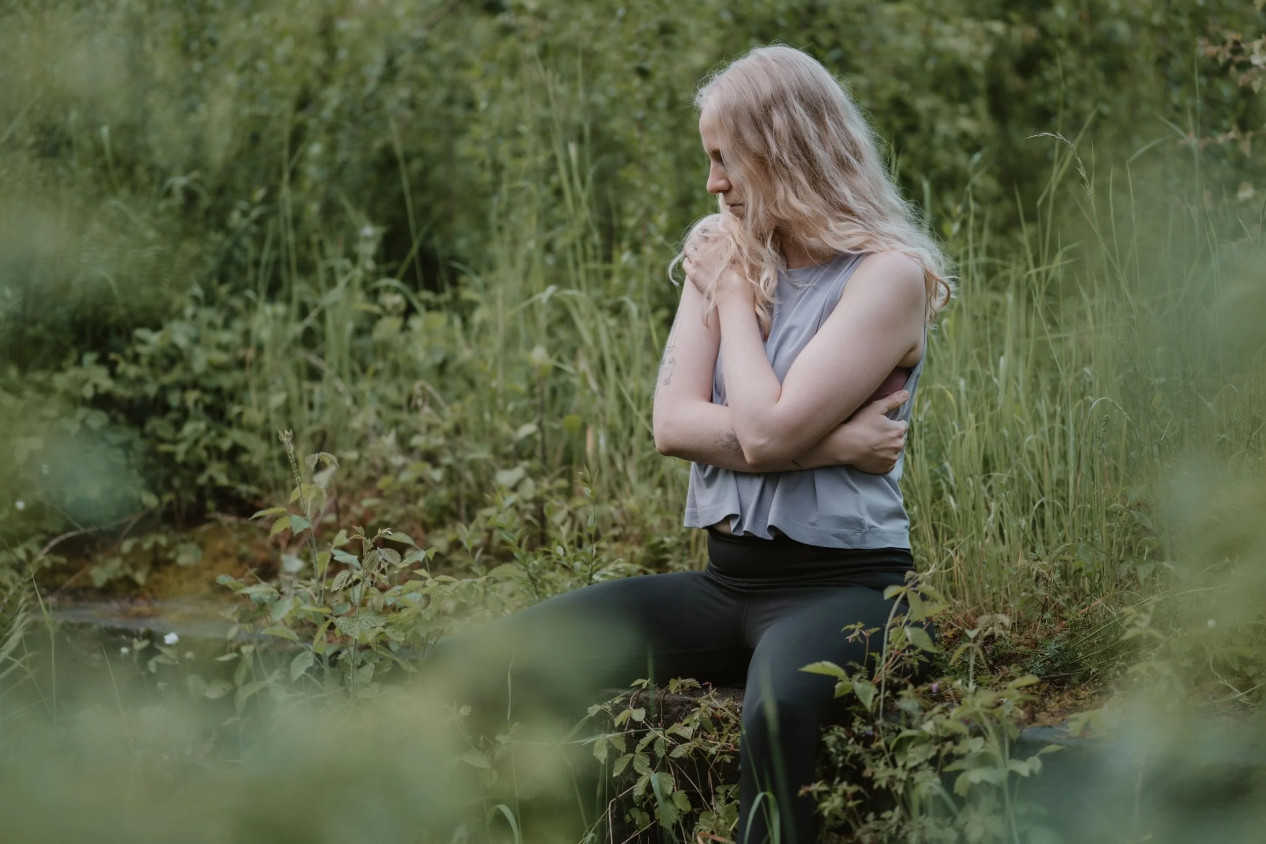 Leona Roes sitzt in der Natur und schenkt sich selbst eine Umarmung als Ausdruck von Mitgefühl und Wohlwollen.