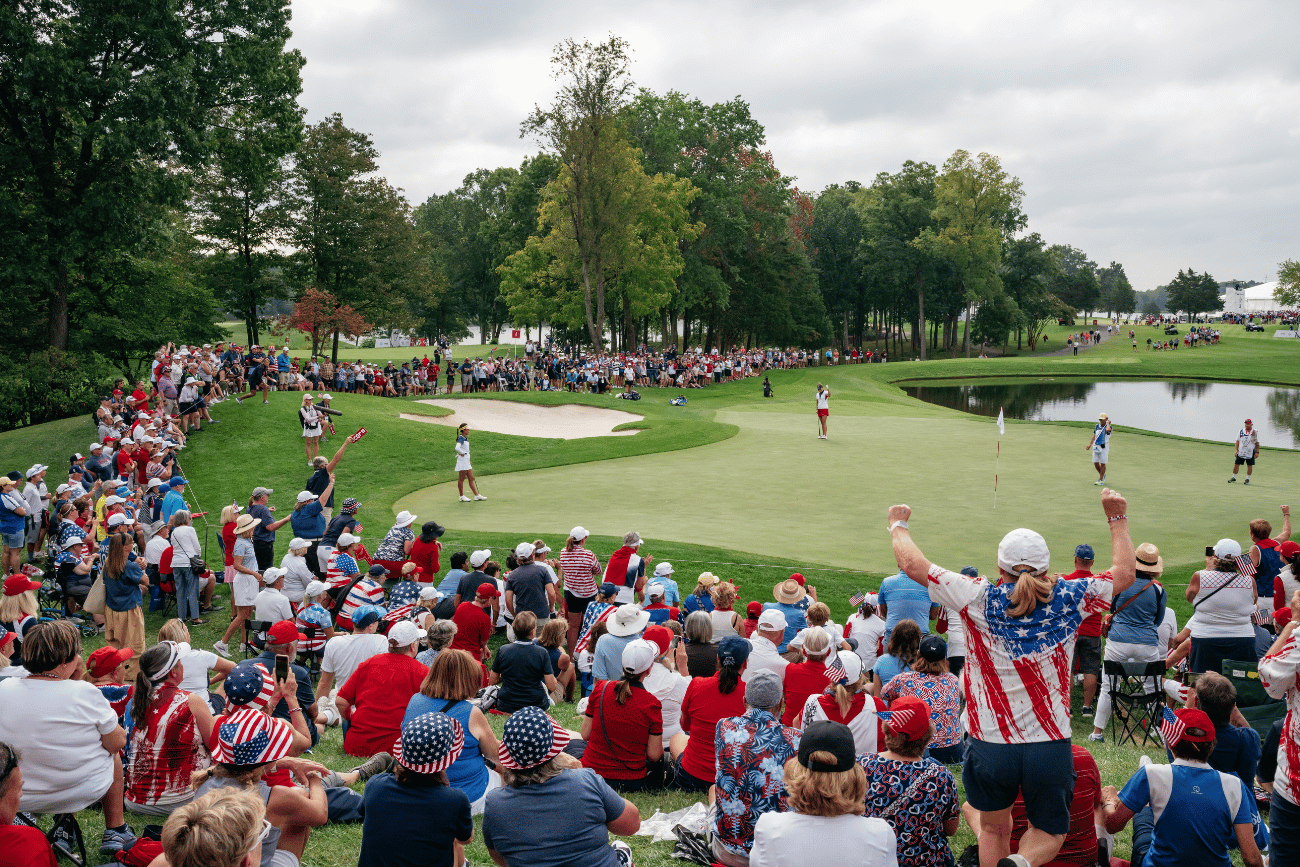 A scenic view of a golf course near a beach with sand dunes, grassy areas, and the ocean in the background under a clear sky.