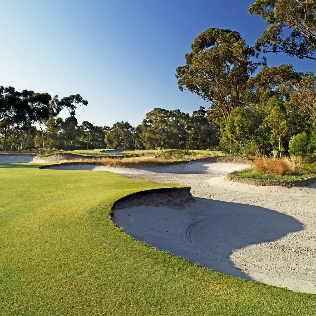 Aerial view of a coastal golf course on a narrow peninsula, with the ocean on one side and water along the other, under a clear sky at sunset.