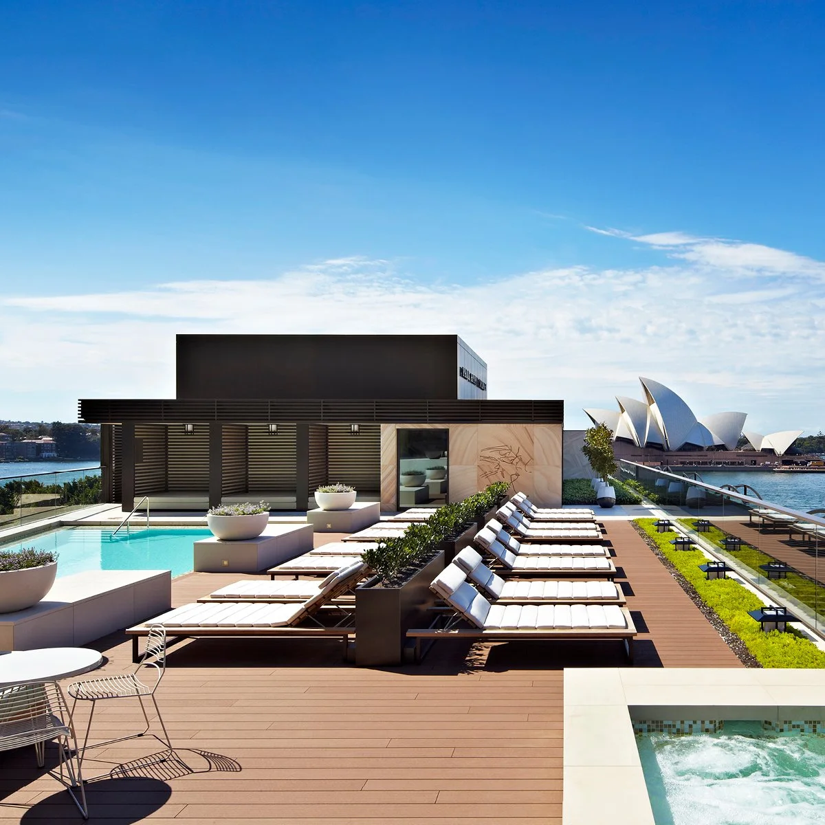 Sydney Opera House with people sitting and walking along the waterfront, under a blue sky with clouds.