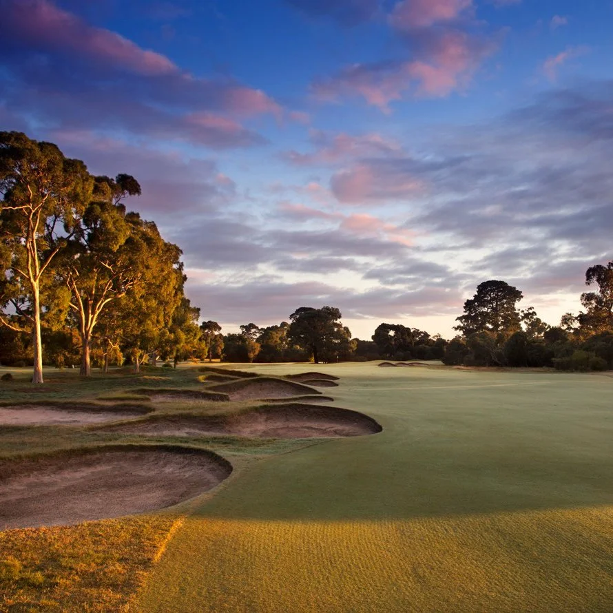 Golf course with sand bunkers, green grass, and trees at sunset under a cloudy sky.