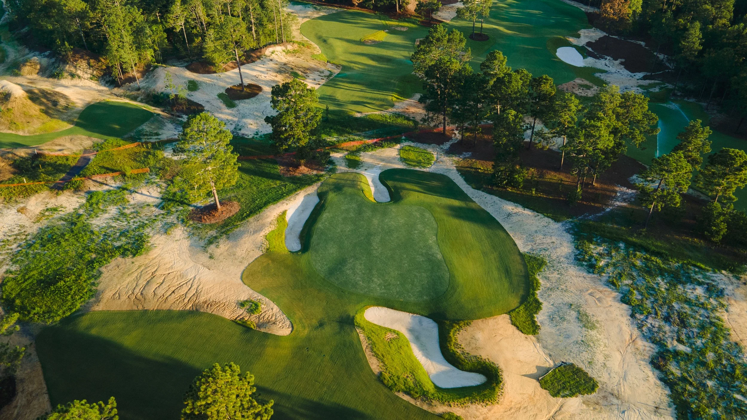 Aerial view of a golf course with sand traps, green fairways, and trees surrounding the area.