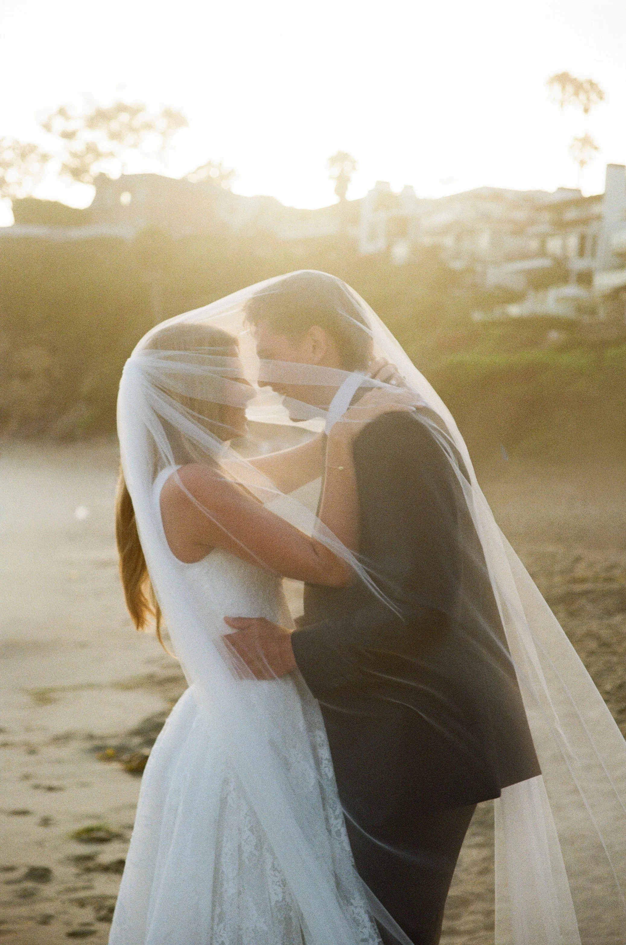 35mm film photo of bride and groom under a veil on the beach in southern california
