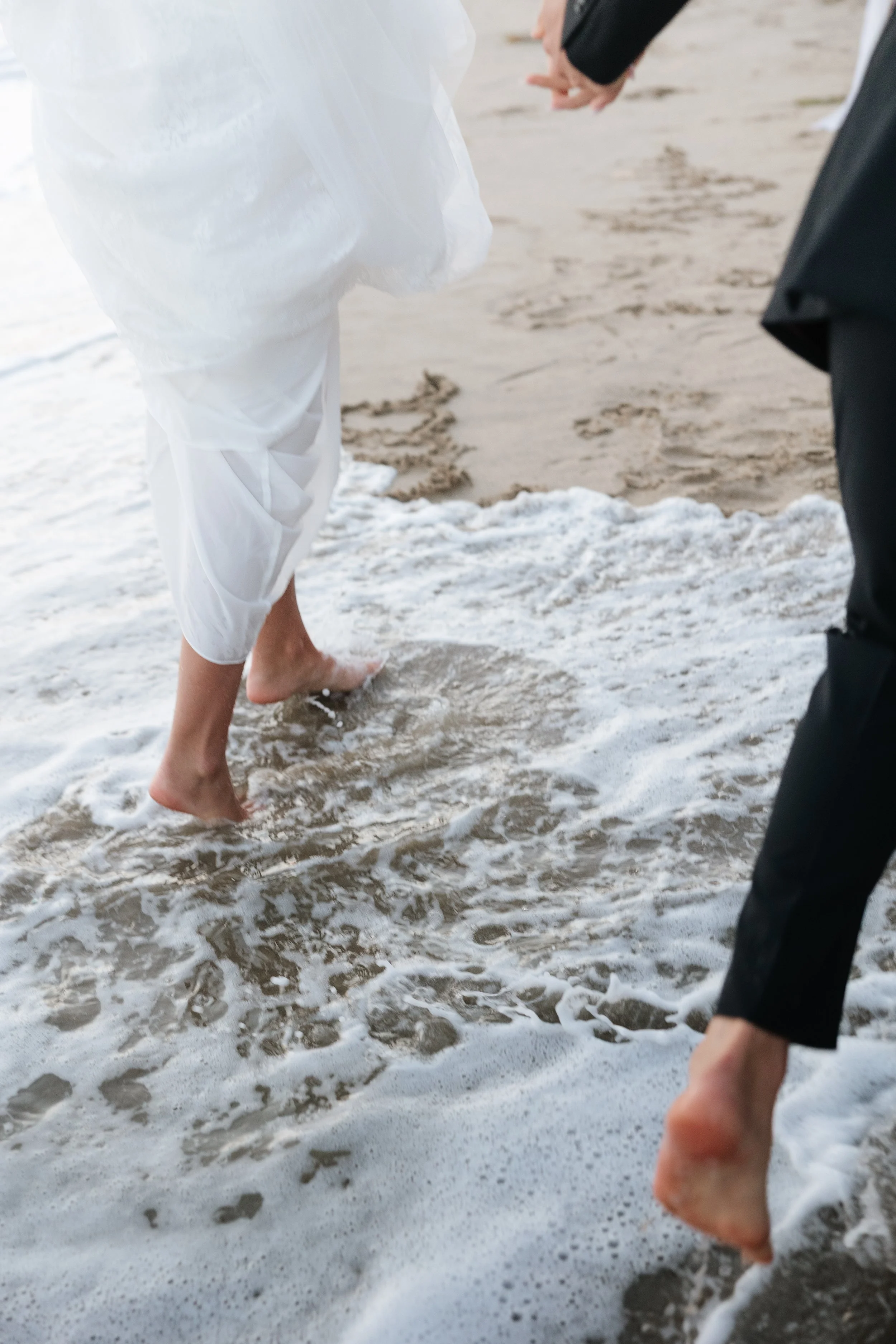 close up photo of bride and groom running through the water on the beach in southern california during their bridal photos