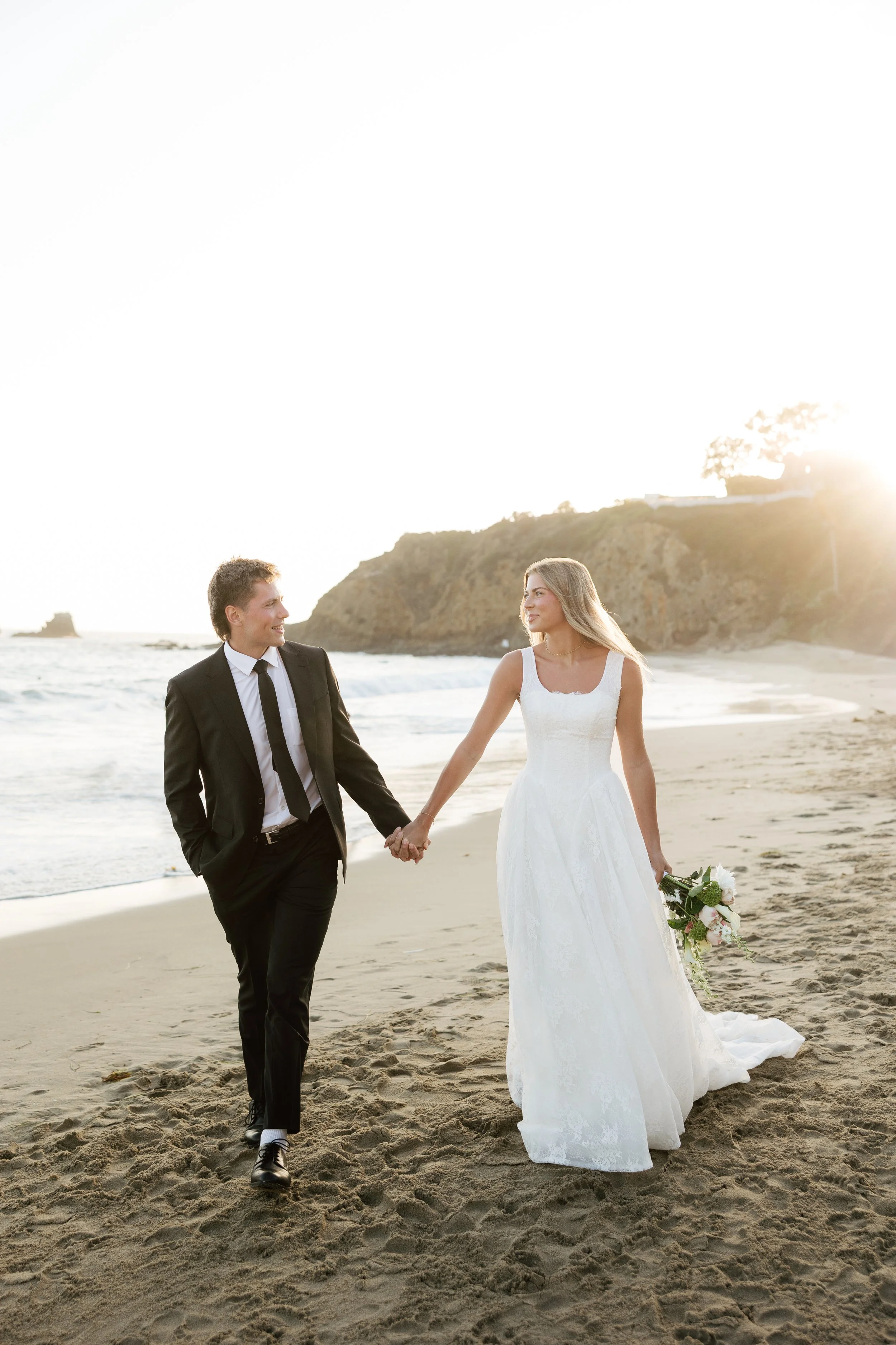 bride and groom walking on the beach while getting their wedding photos taken
