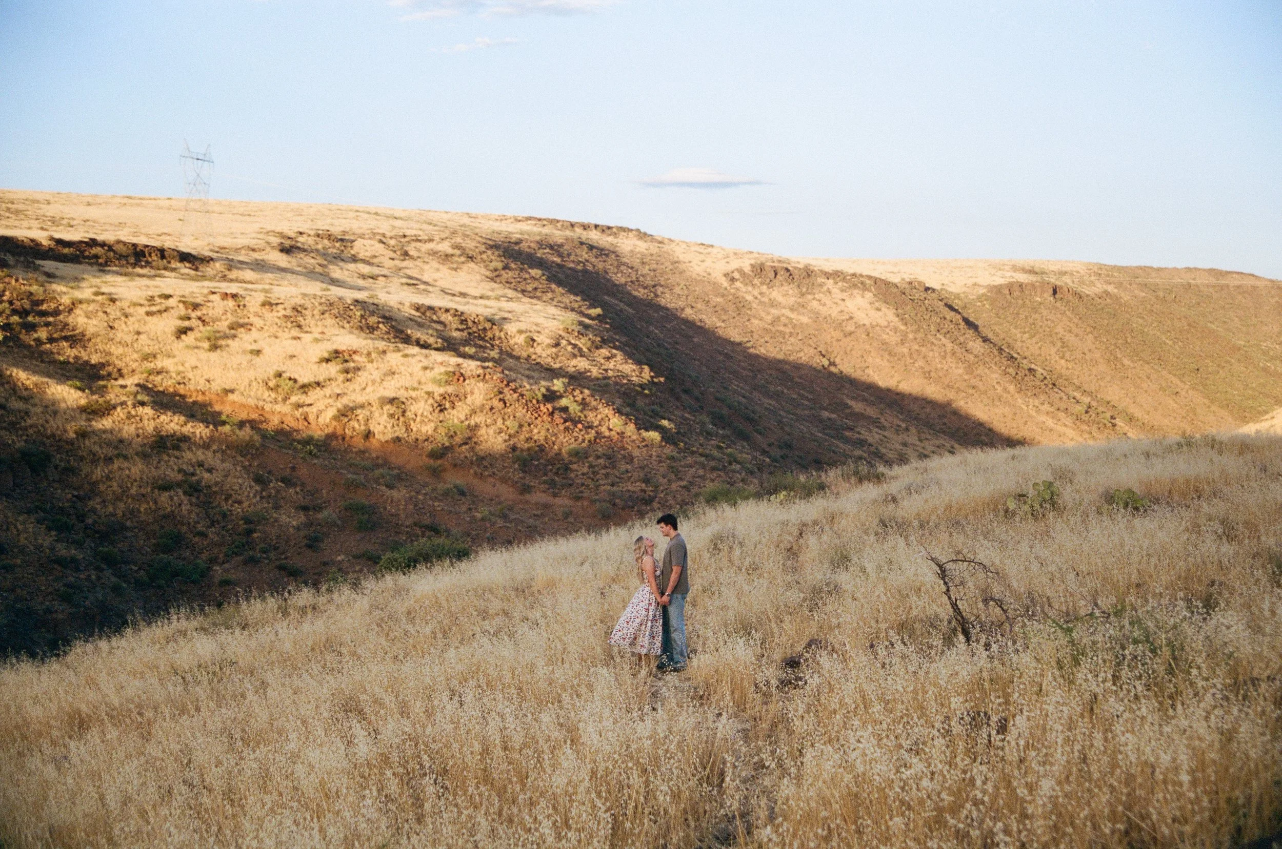 35mm film photograph of an engaged couple standing together in golden Arizona grasslands at sunset.