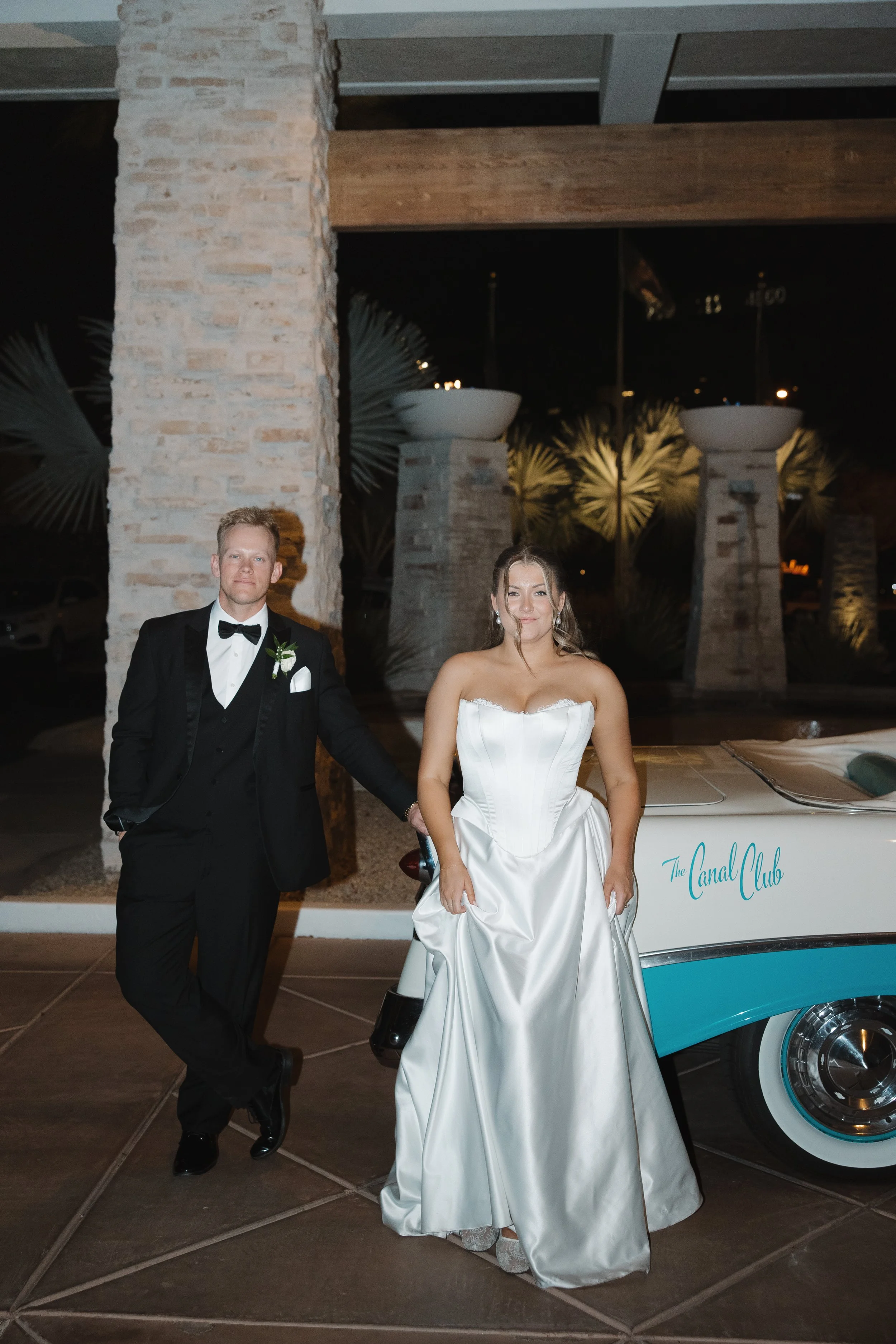 Bride and groom leaning against vintage car outside The Canal Club at The Scott Resort & Spa in Scottsdale, Arizona