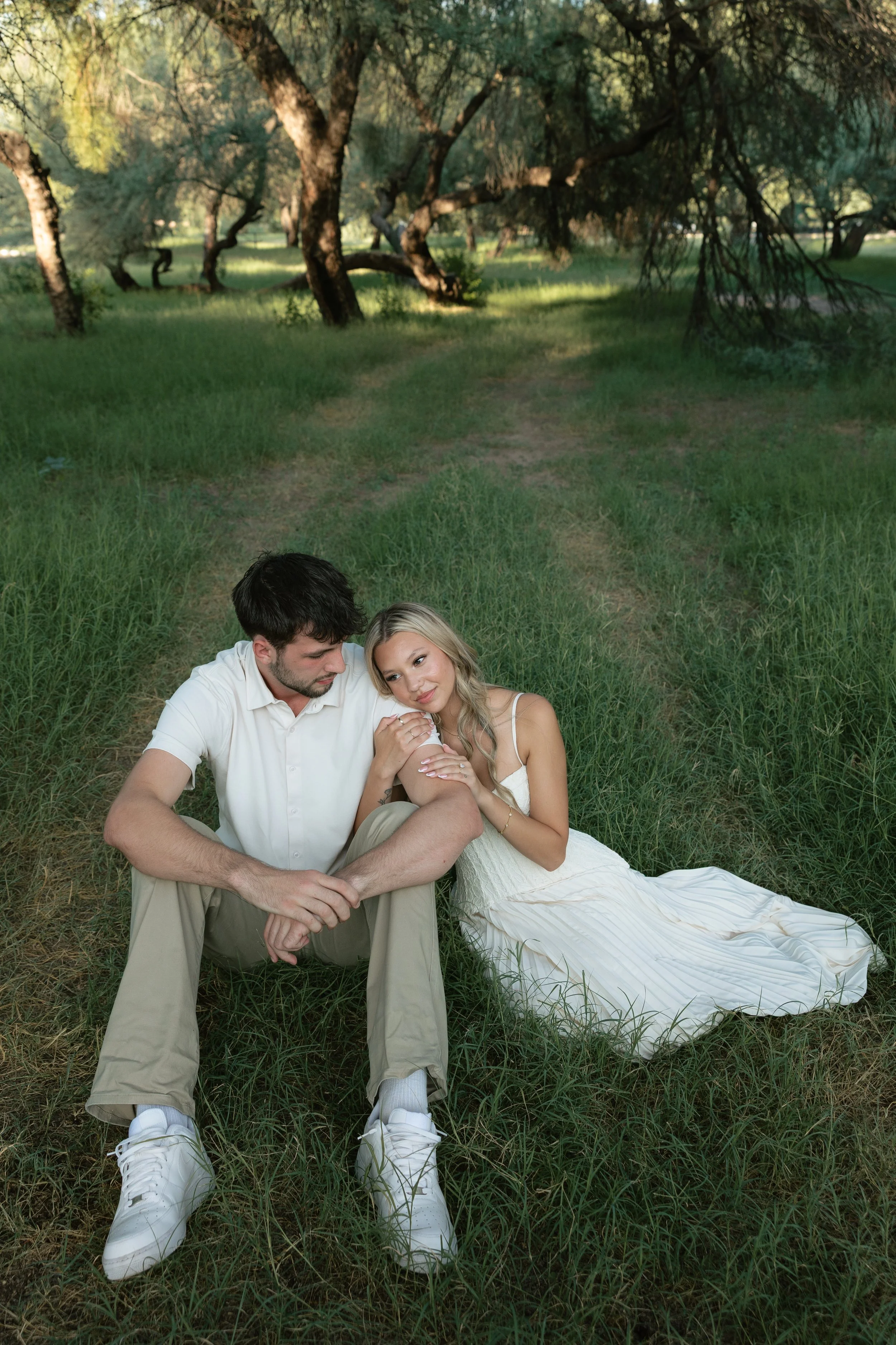 engaged couple sitting on the ground in a green field in the summer in arizona at saguaro lake