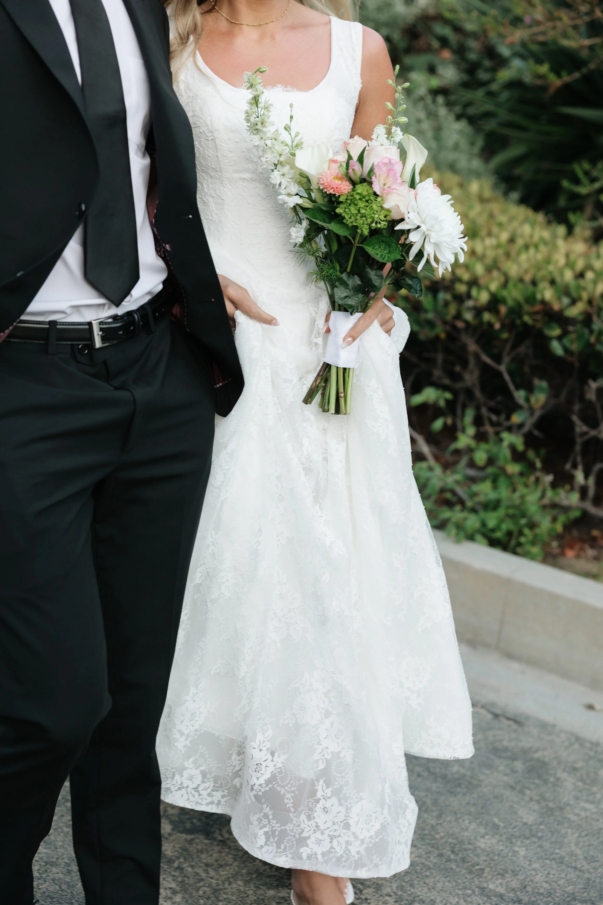 details of bride and groom attire close up photo of brides dress and grooms suit with floral bouquet